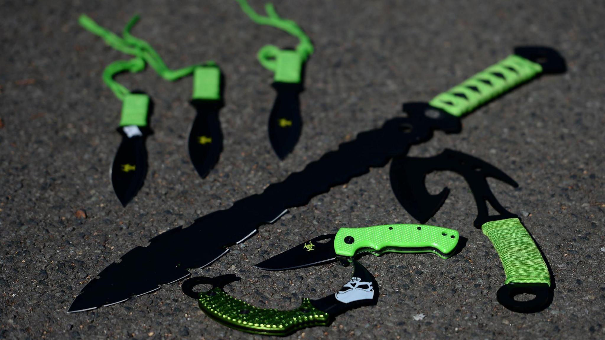 Some examples of 'zombie knives' at a secure police location. The knives have various sized blades and green handles, including a large knife with a serrated edge. 
