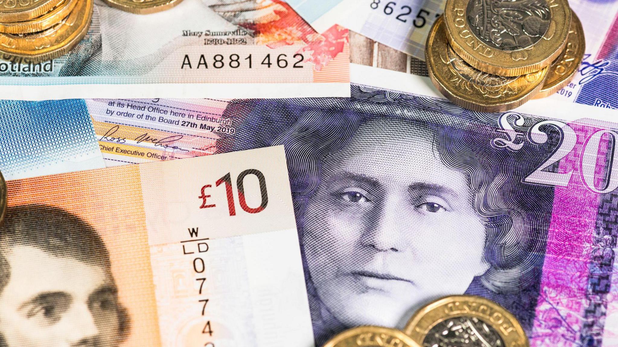 £5, £10 and £20 notes scattered on a surface with piles of £1 coins on top