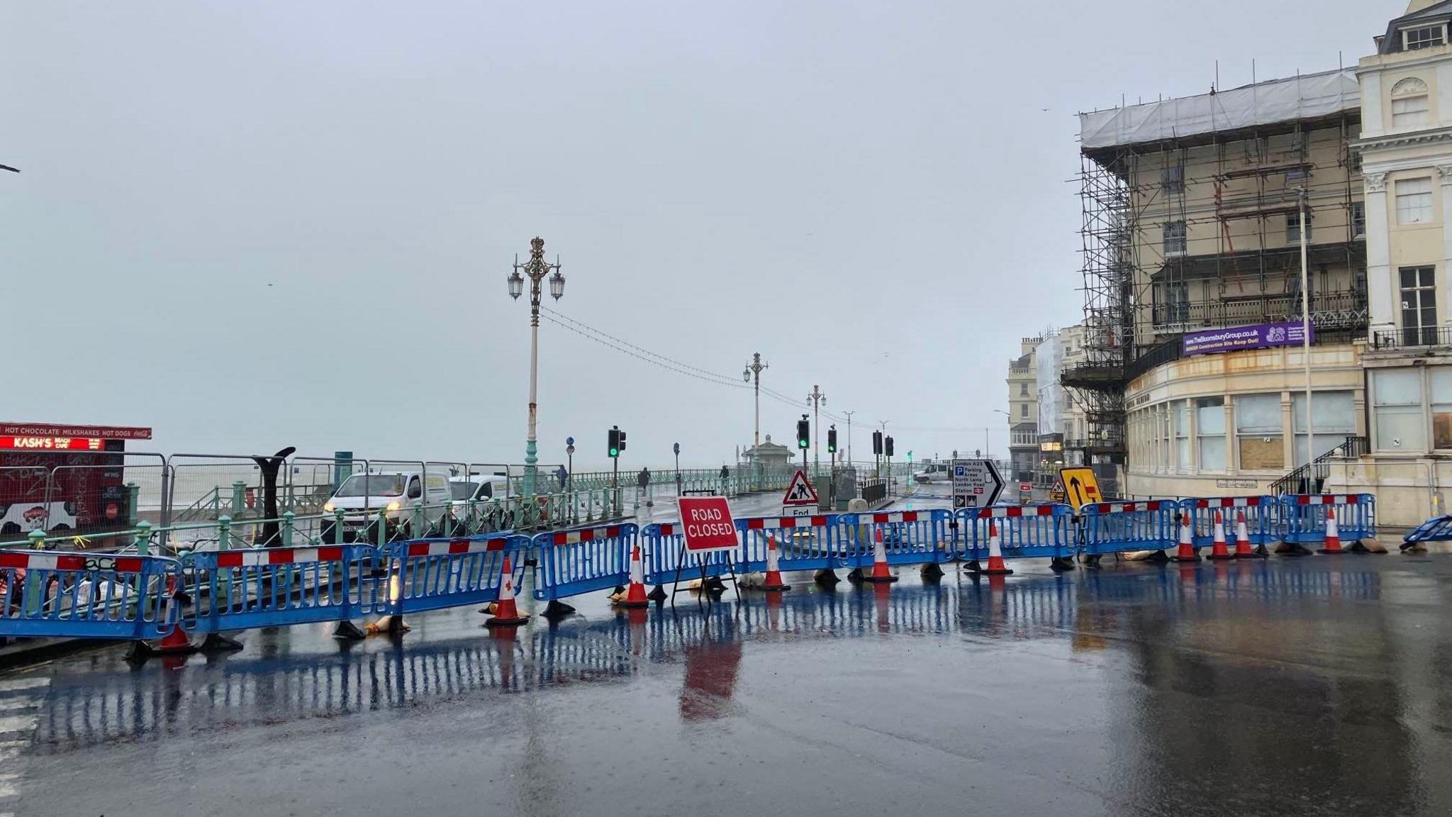 A view of the hotel from the road which shows half of the building missing and the other half covered in scaffolding. There are blue barriers across the road leading to the hotel.