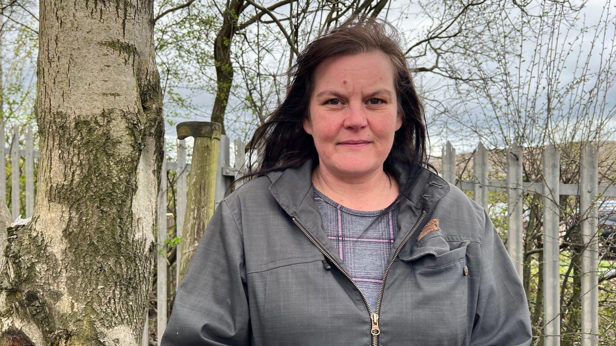 Rebecca Currie, a woman wearing a grey coat is stood against a set of metal railings.