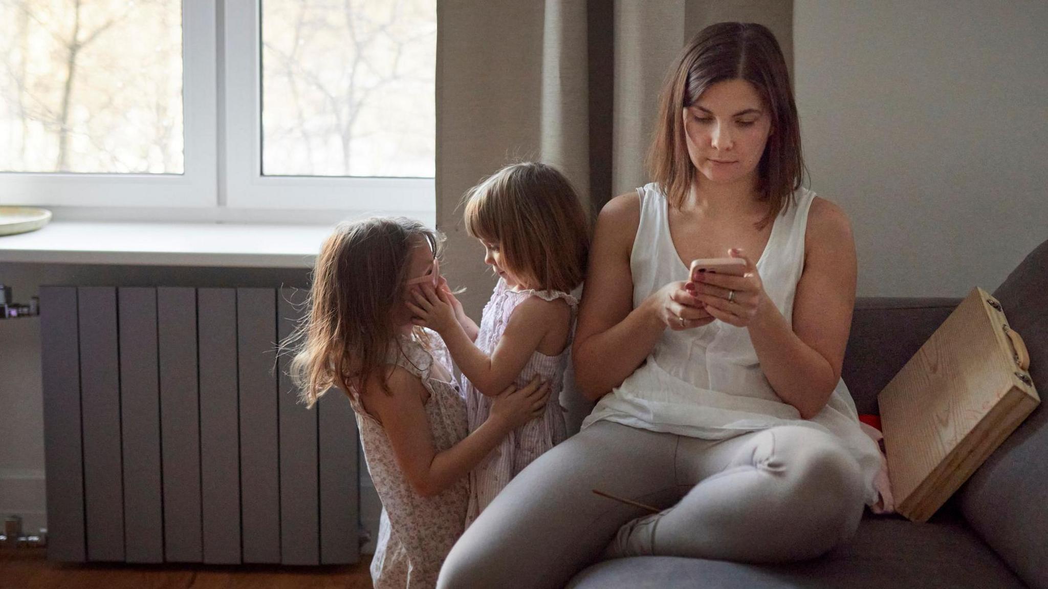 Mother with two daughters at home using mobile phone