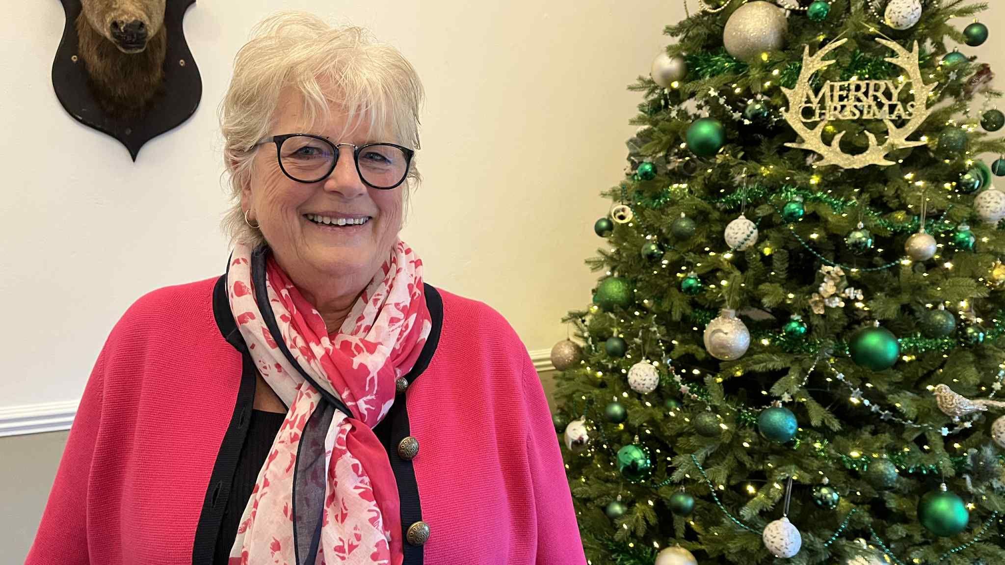 Lyn Roberts yn sefyll o flaen coeden Nadolig