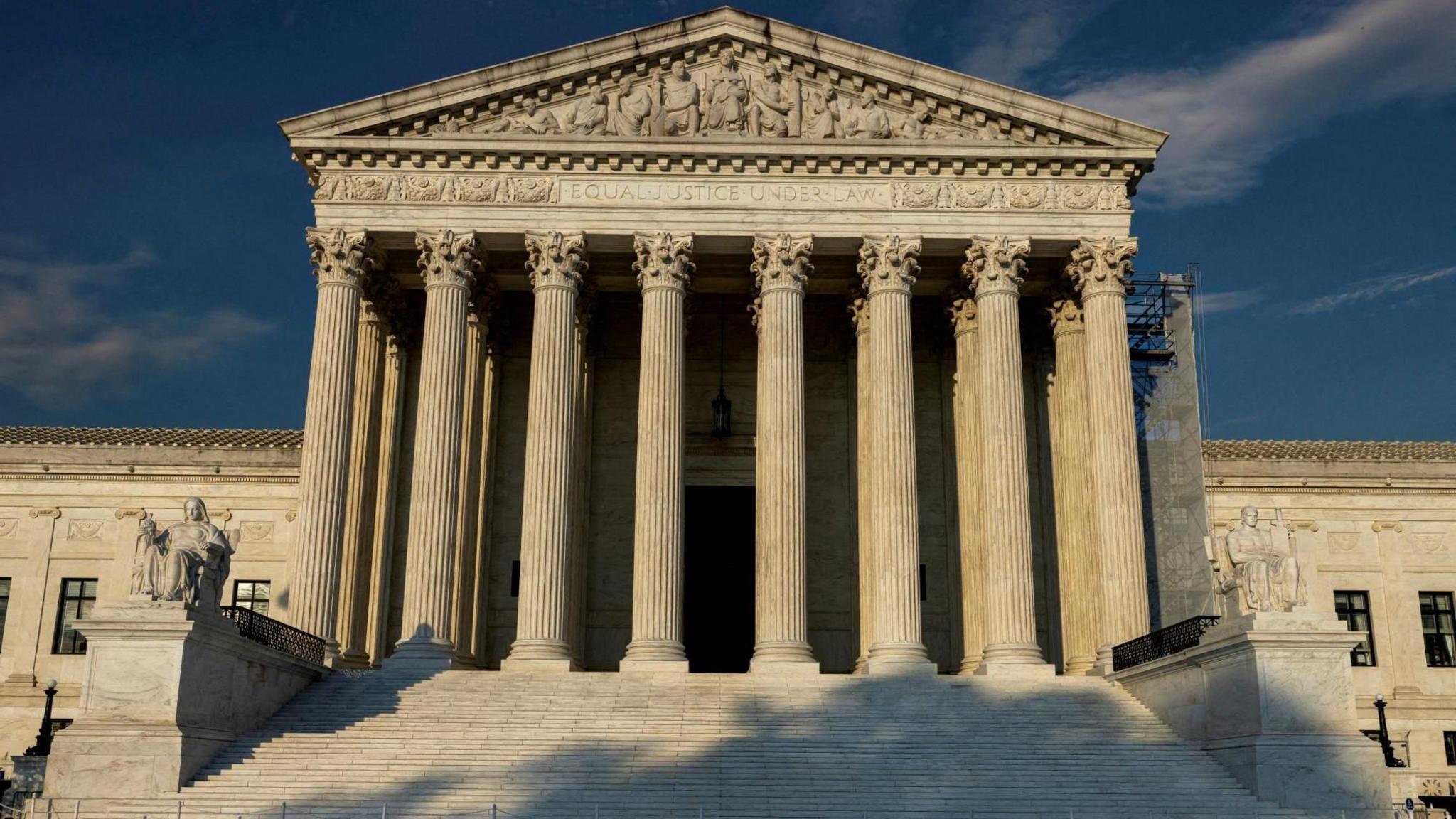 An exterior view of the US Supreme Court building's columned entrance in Washington DC with sunlight shining on it.