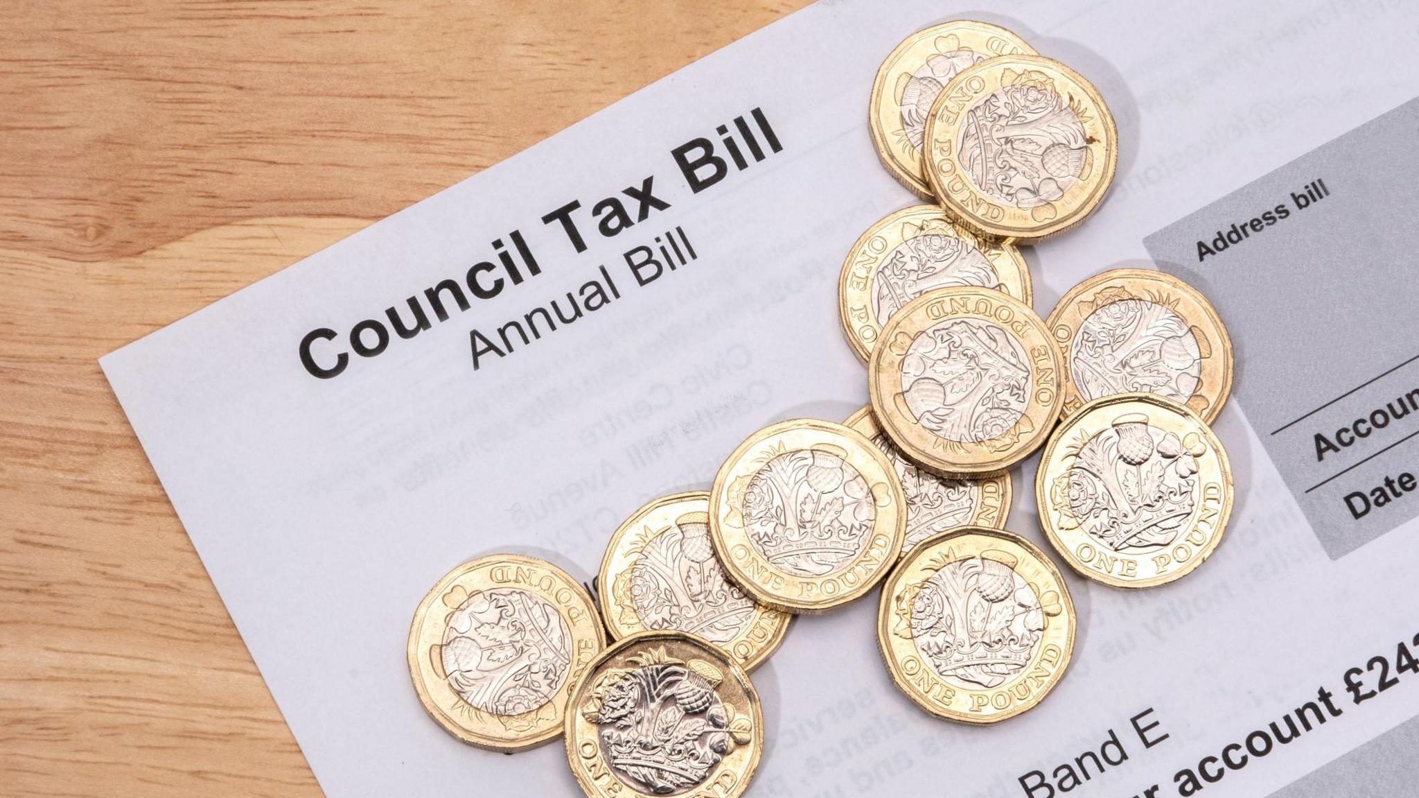 A photo of a council tax annual bill on a wooden surface. Several British £1 coins are laid on top of the piece of paper.