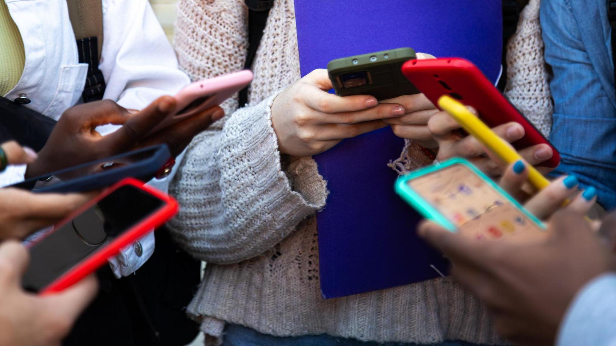 Young people stand in a circle looking down at phones they are holding
