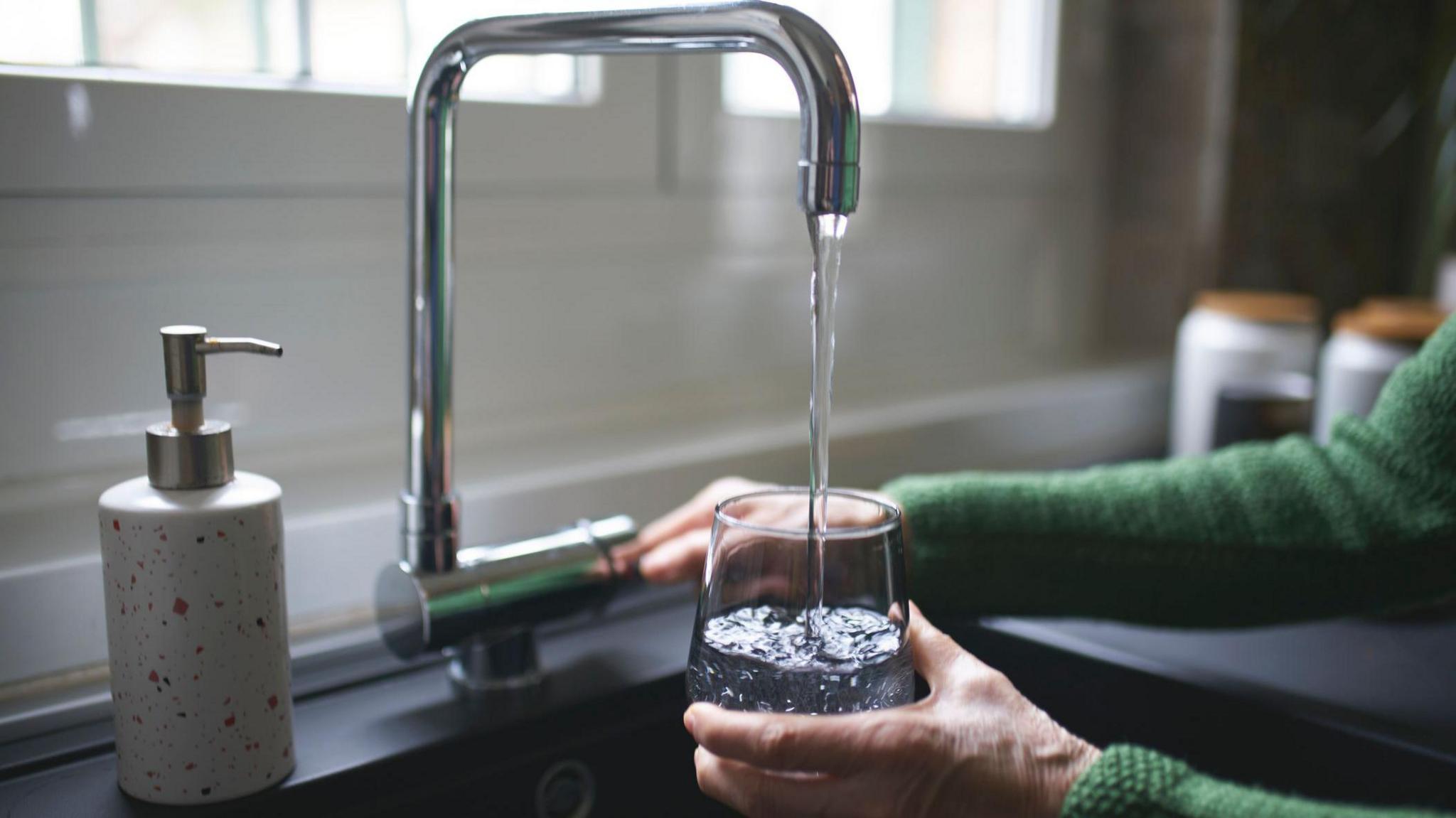 A glass is held under and tap in a kitchen and is being filled with water