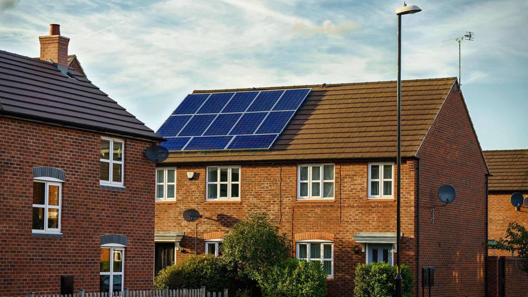 blue solar panels on the roof of a red brick house.