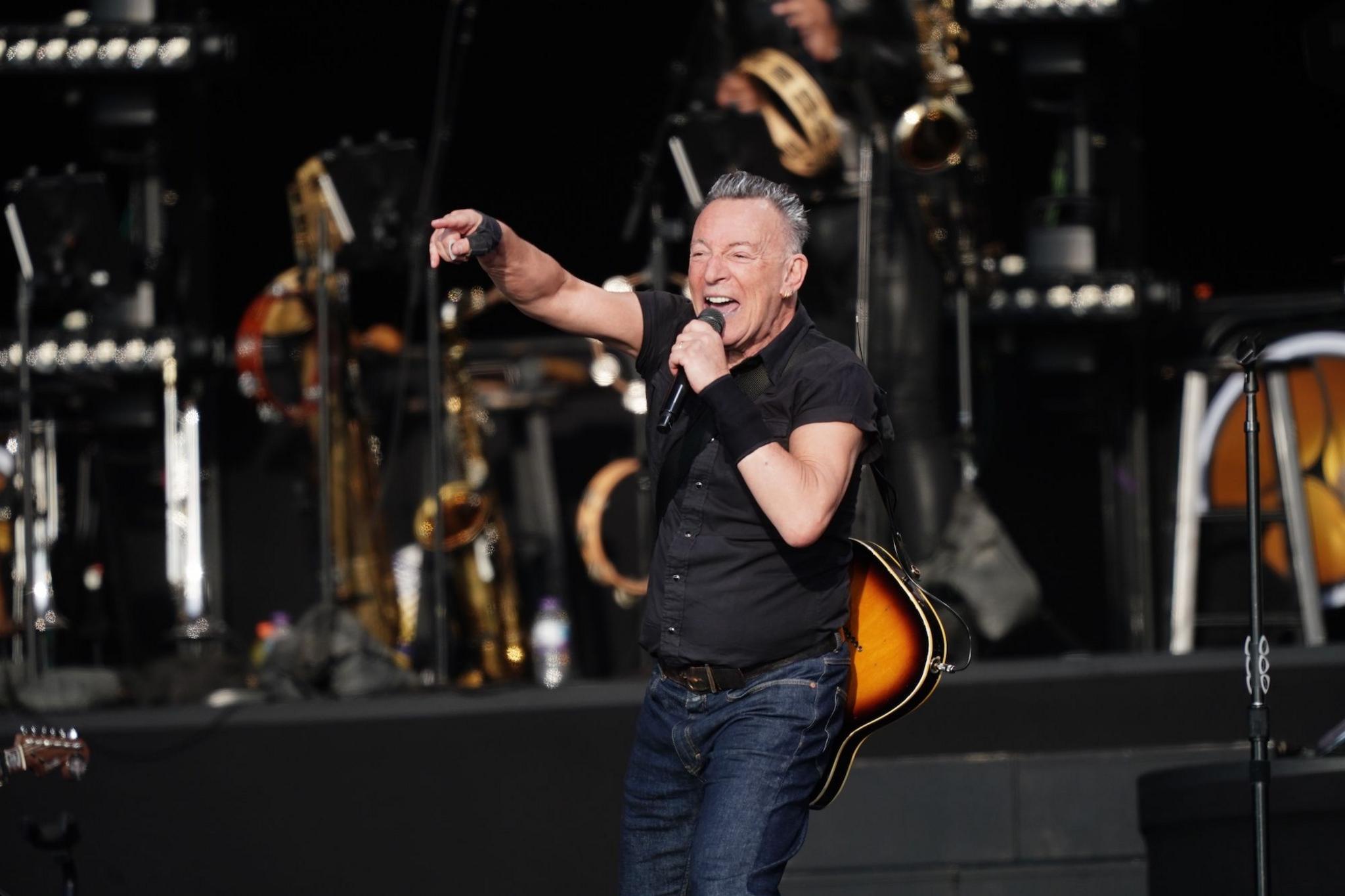 Bruce Springsteen plays at the BST Hyde Park festival in London, 2023. He is pointing at the crowd while singing. He is wearing a black shirt and dark denim jeans.