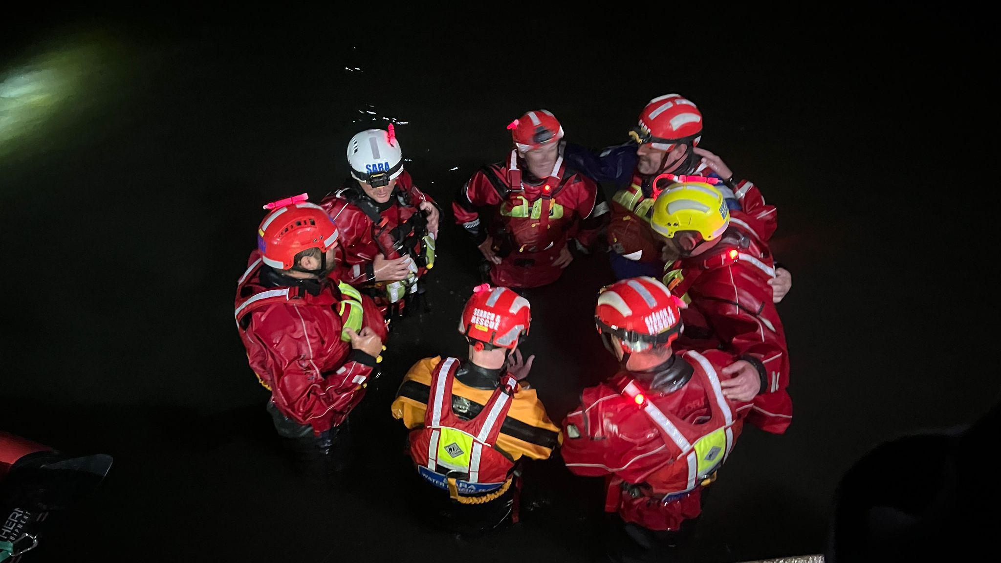Seven of the 10 volunteers are standing shoulder to shoulder together in a circle, wearing red overalls. All are wearing helmets - five are red, one is white and the last is yellow. They are standing in the pitch black.