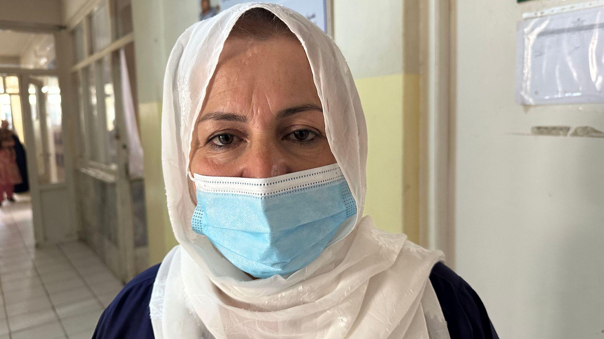 A head-and-shoulders portrait of Razia Hanifi wearing a white head scarf and medical mouth covering in a corridor on the hospital's ward.