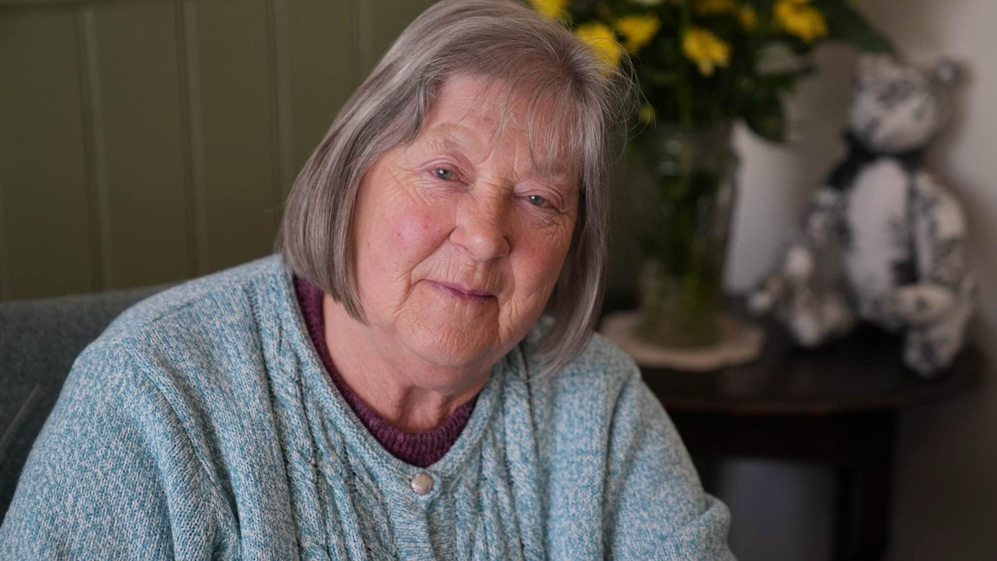 Joan James wearing a blue cardigan while looking into the camera. Her head is slightly tilted