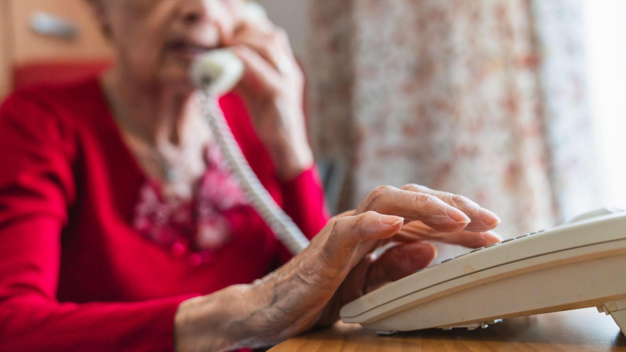 A stock image of an elderly woman using a landline at home