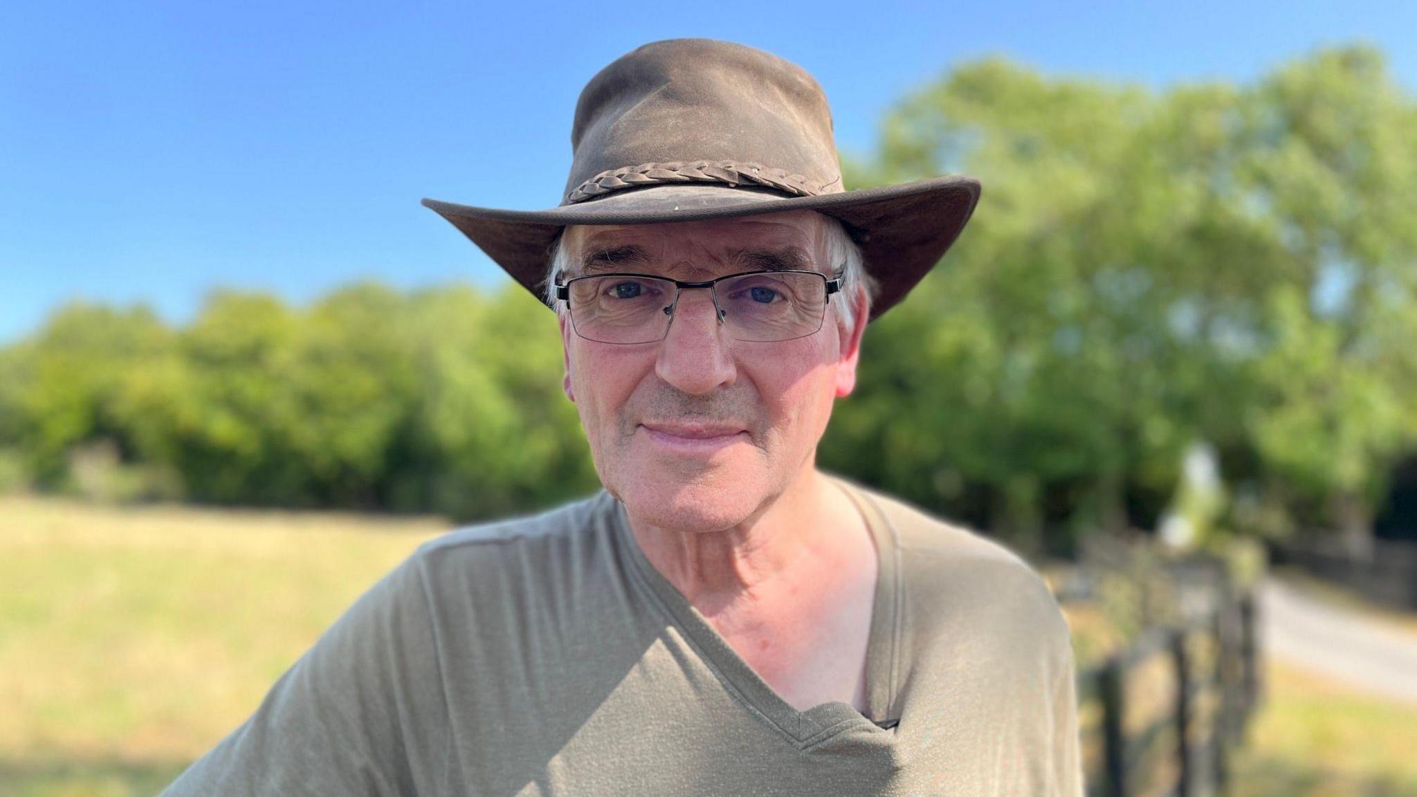 Robert Law at his farm. He is wearing a green T-shirt and a hat and looking directly at the camera. 