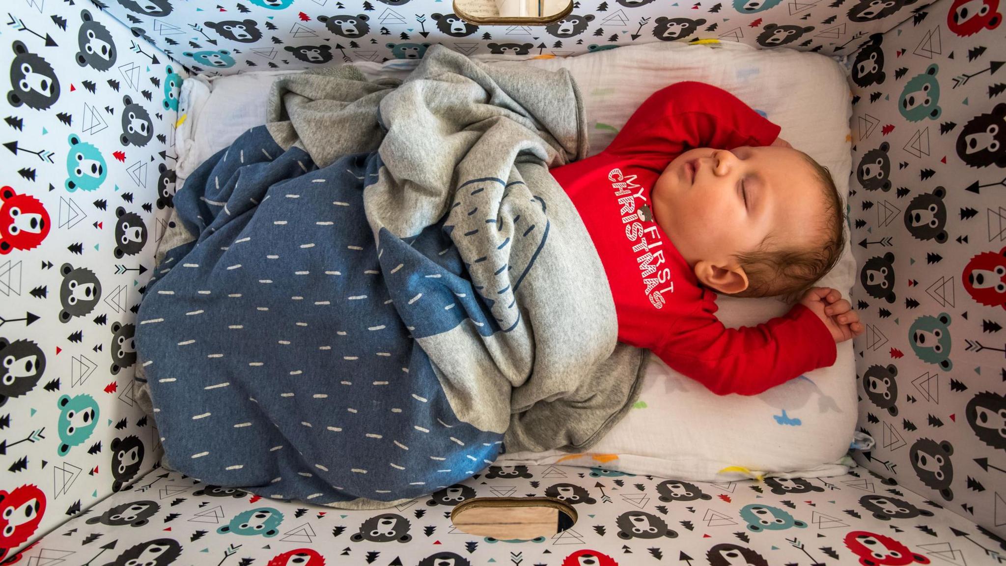 Baby boy with a red outfit sleeping in a Finnish cardboard box.