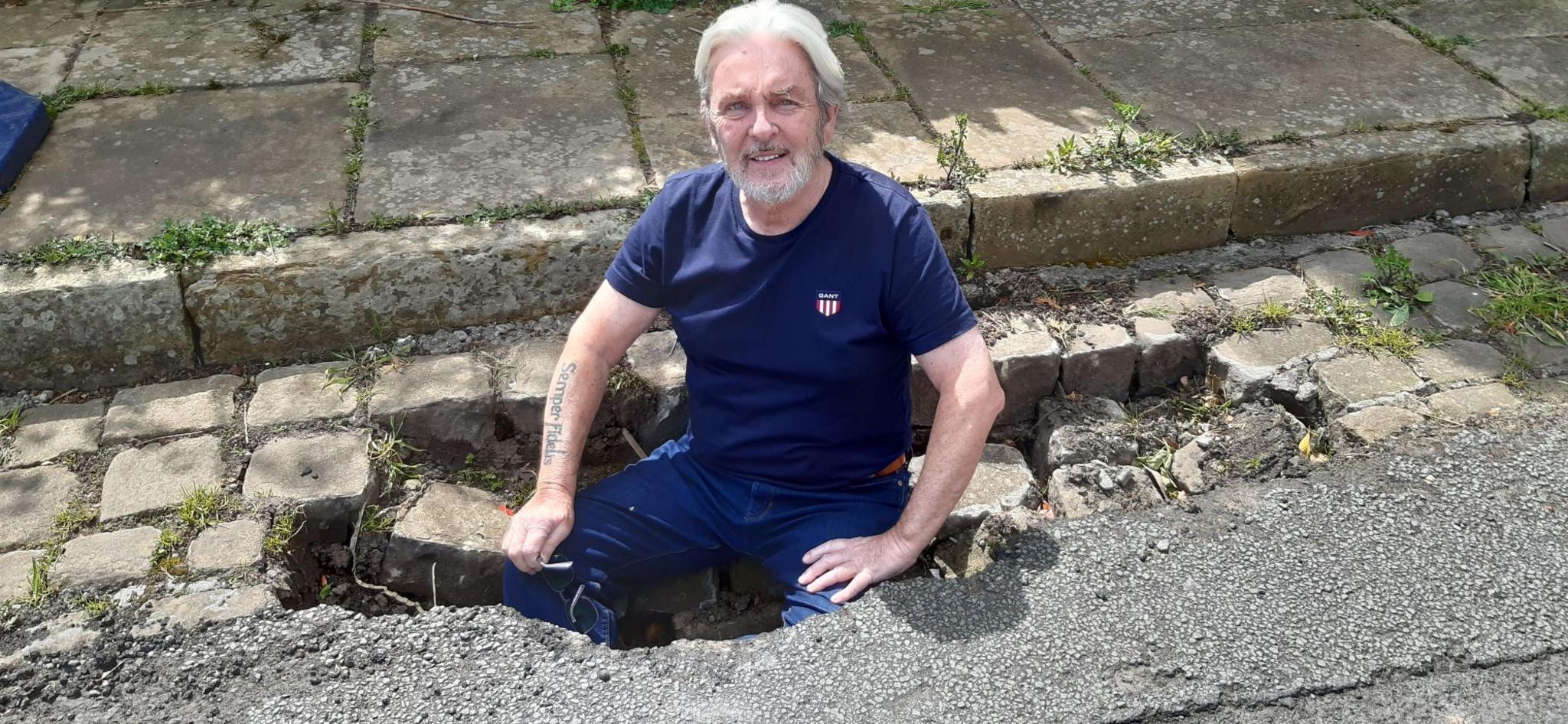 Alan sits on the edge of a pothole with his legs fully inside it.