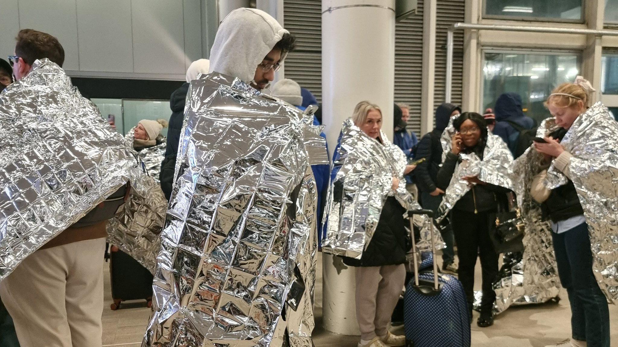 Passengers at Gatwick Airport after an evacuation. They are covered in silver foil heat warmers. 