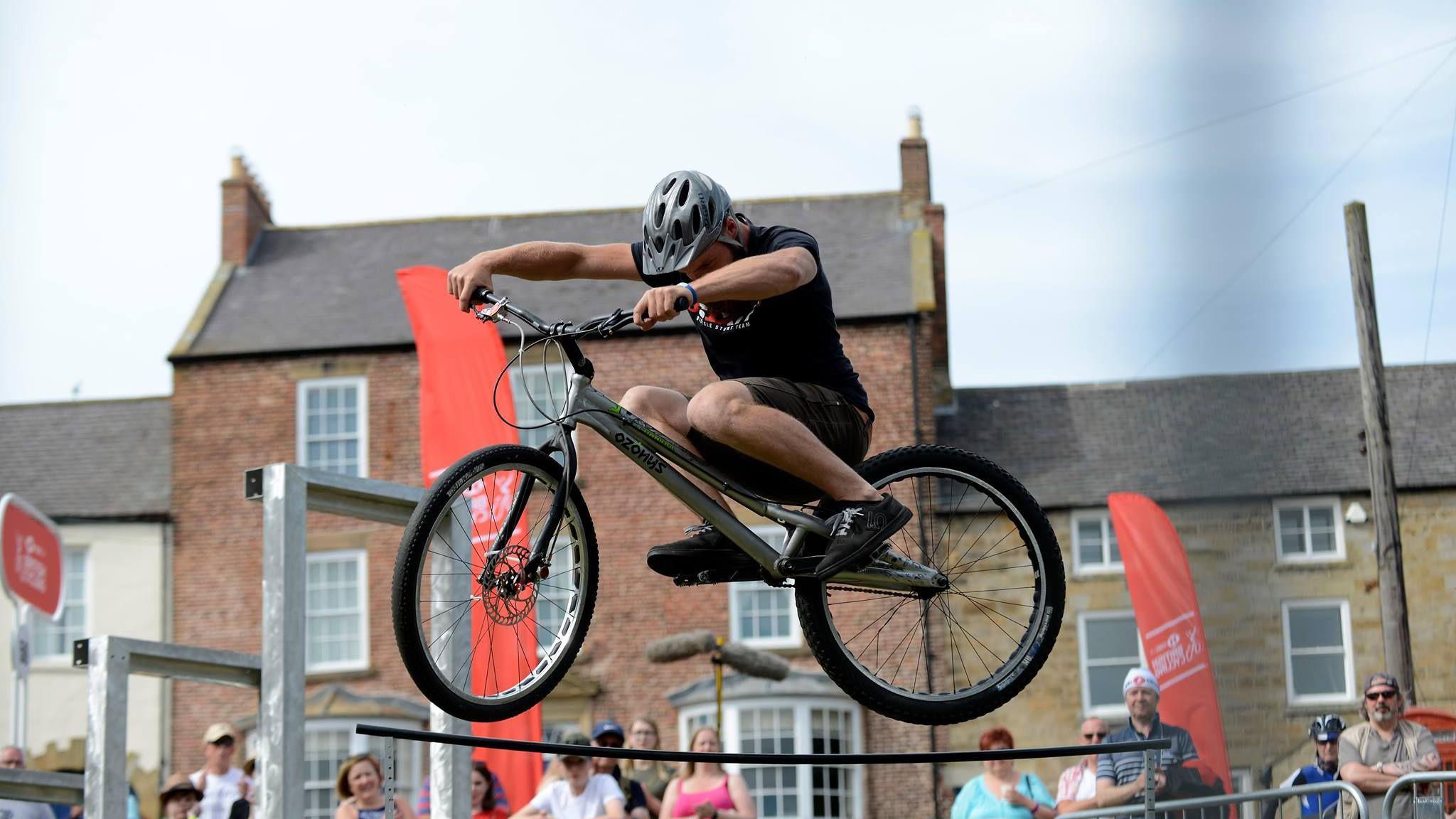 A stunt rider jumping his bike in the air while a crowd watches the show.