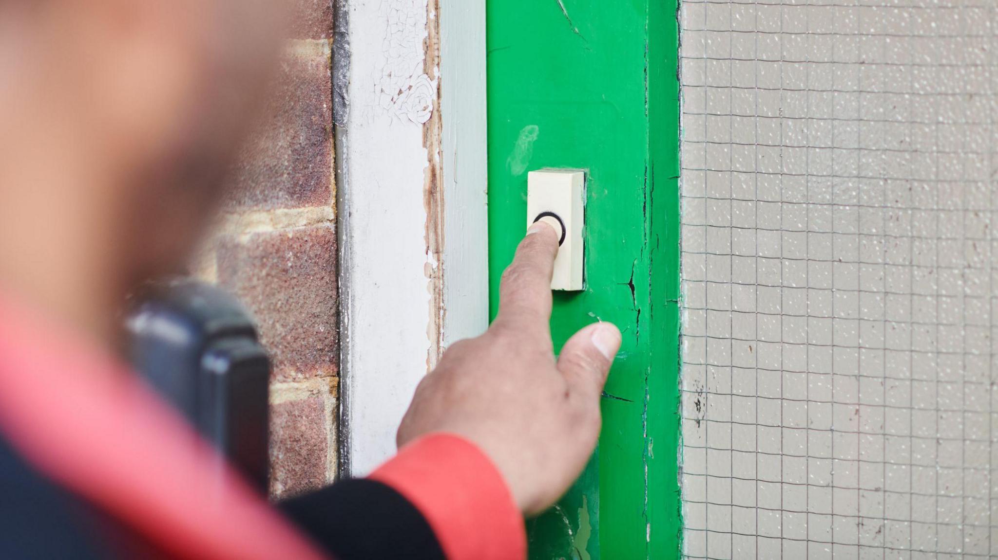 Generic image of a man ringing a doorbell on a green door 