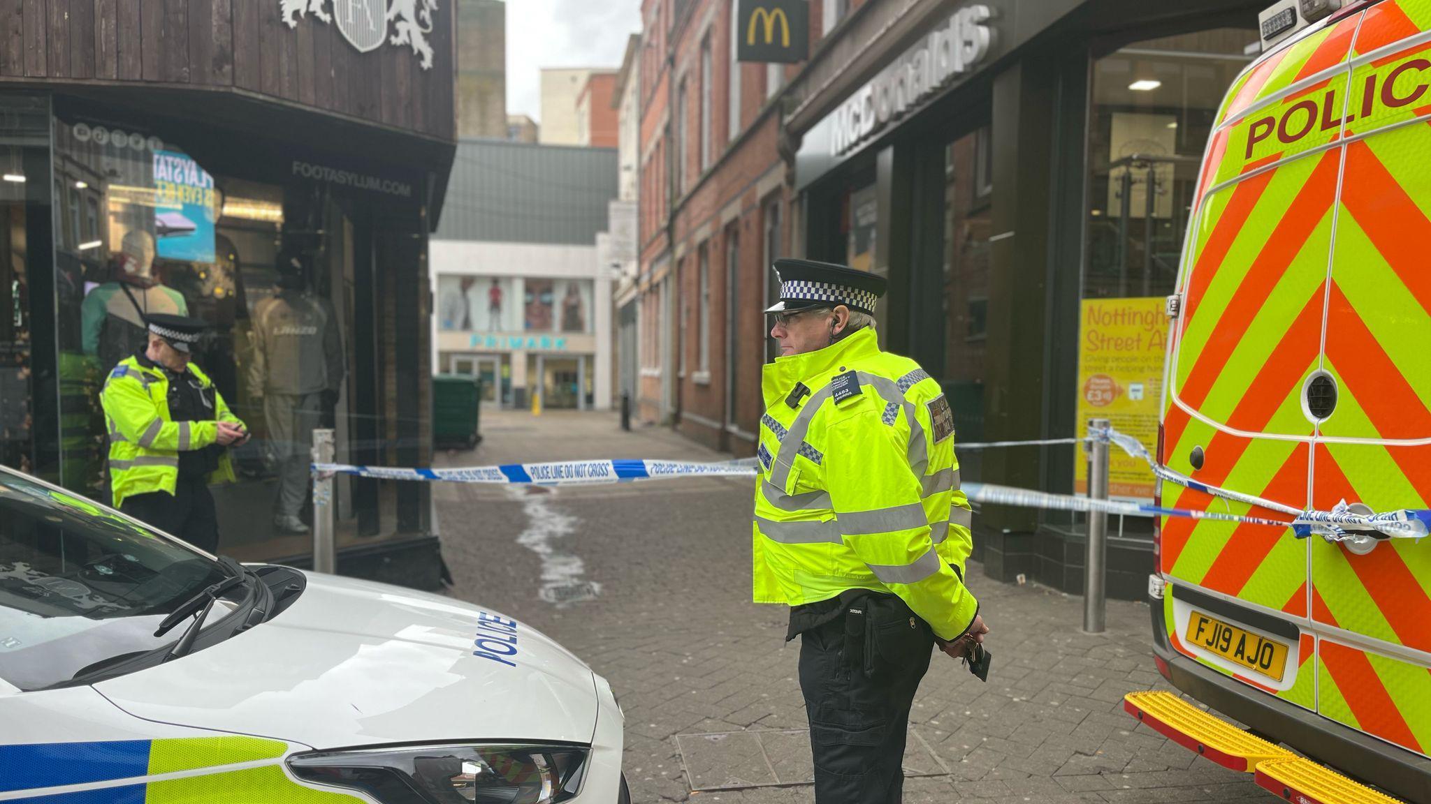 Police vehicles and two officers guard a cordon on an alleyway to Primark