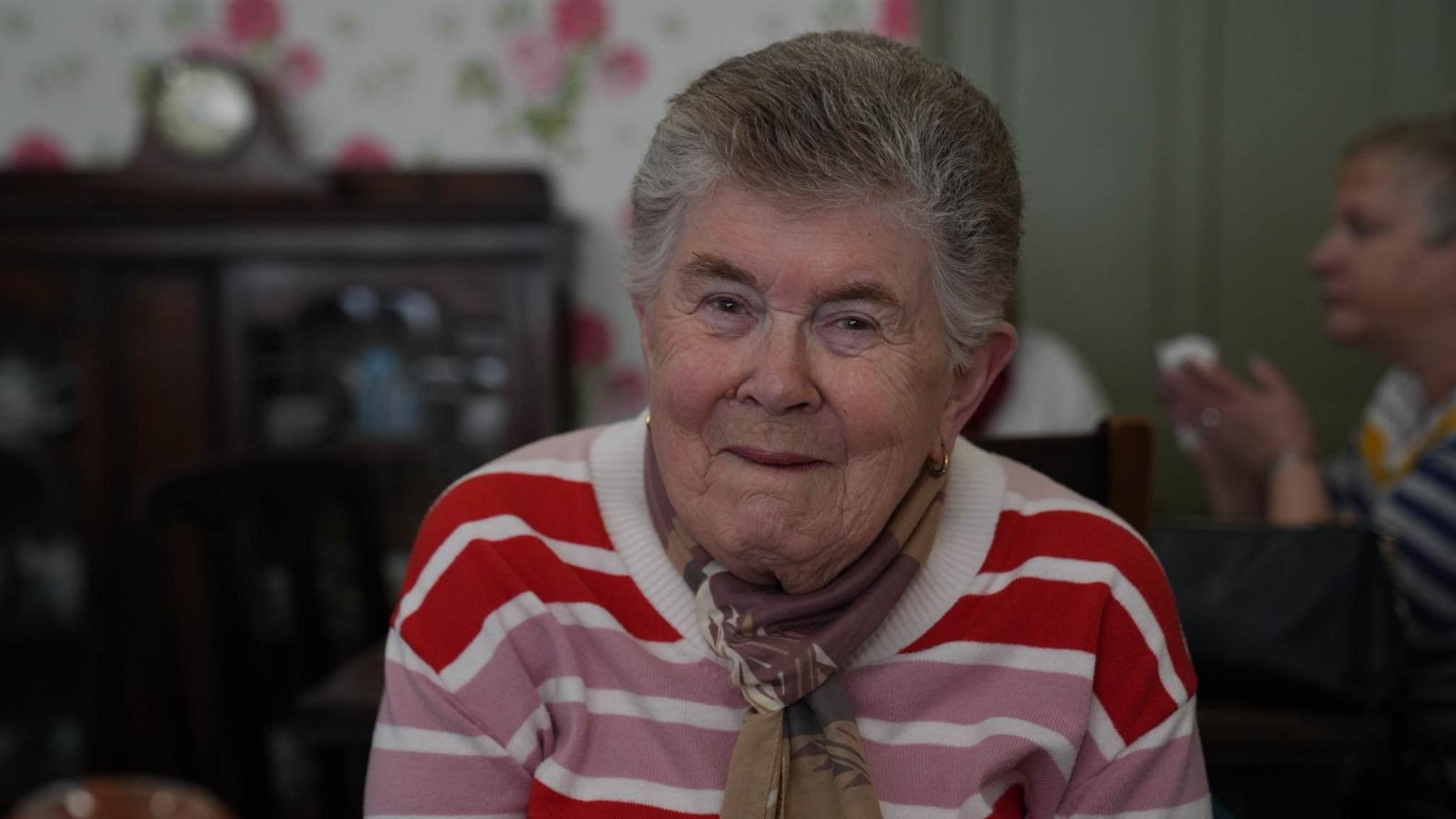 Dorothy King wearing a scarf and a colourful striped jumper looking into the camera 