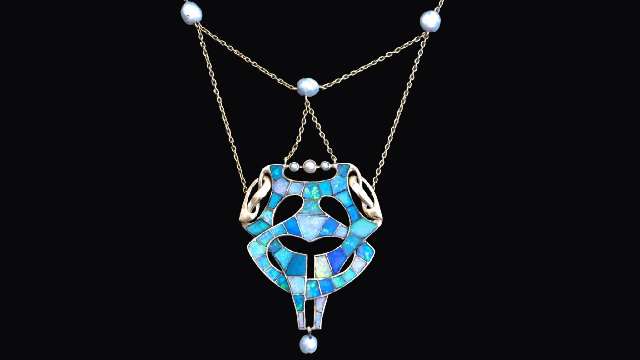 A Knox designed blue mosaic necklace. The pendant is blue and silver, is rounded and has different elements that interlock with each other.