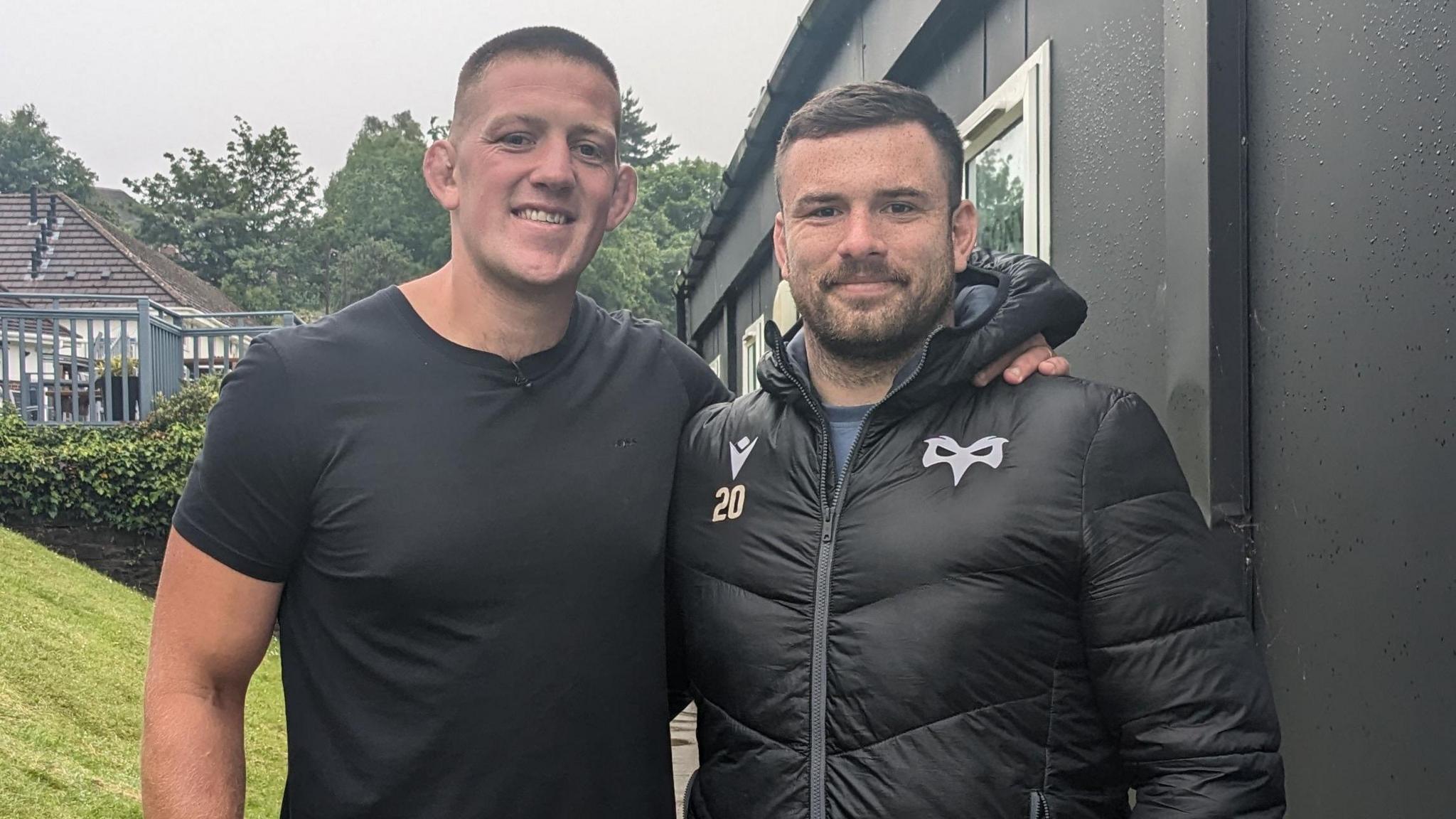 Lloyd Ashley with a fellow player, hugging. Both wearing black. 