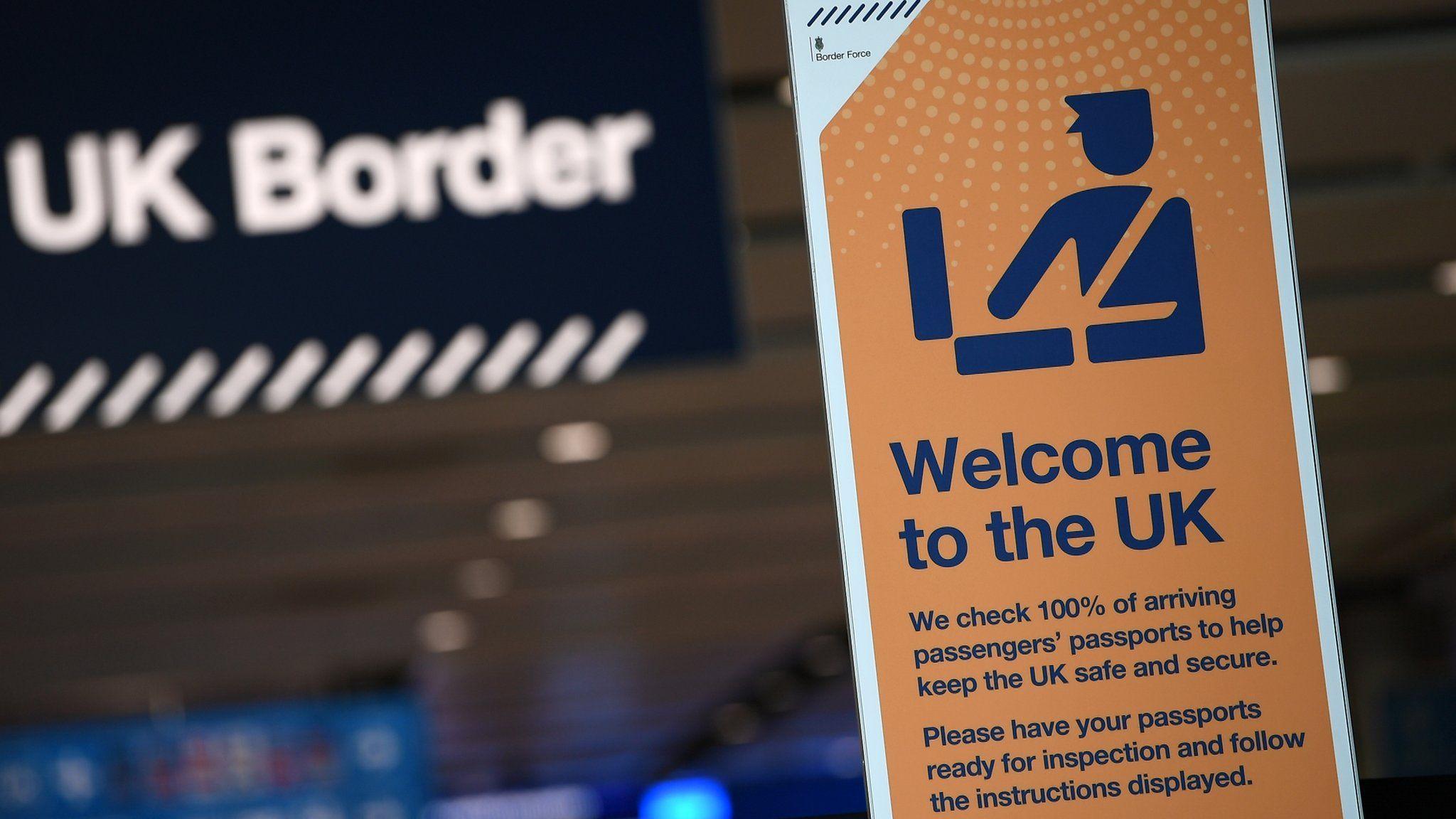 An orange sign at the UK border that says "welcome to the UK" and advises people of passport checks.