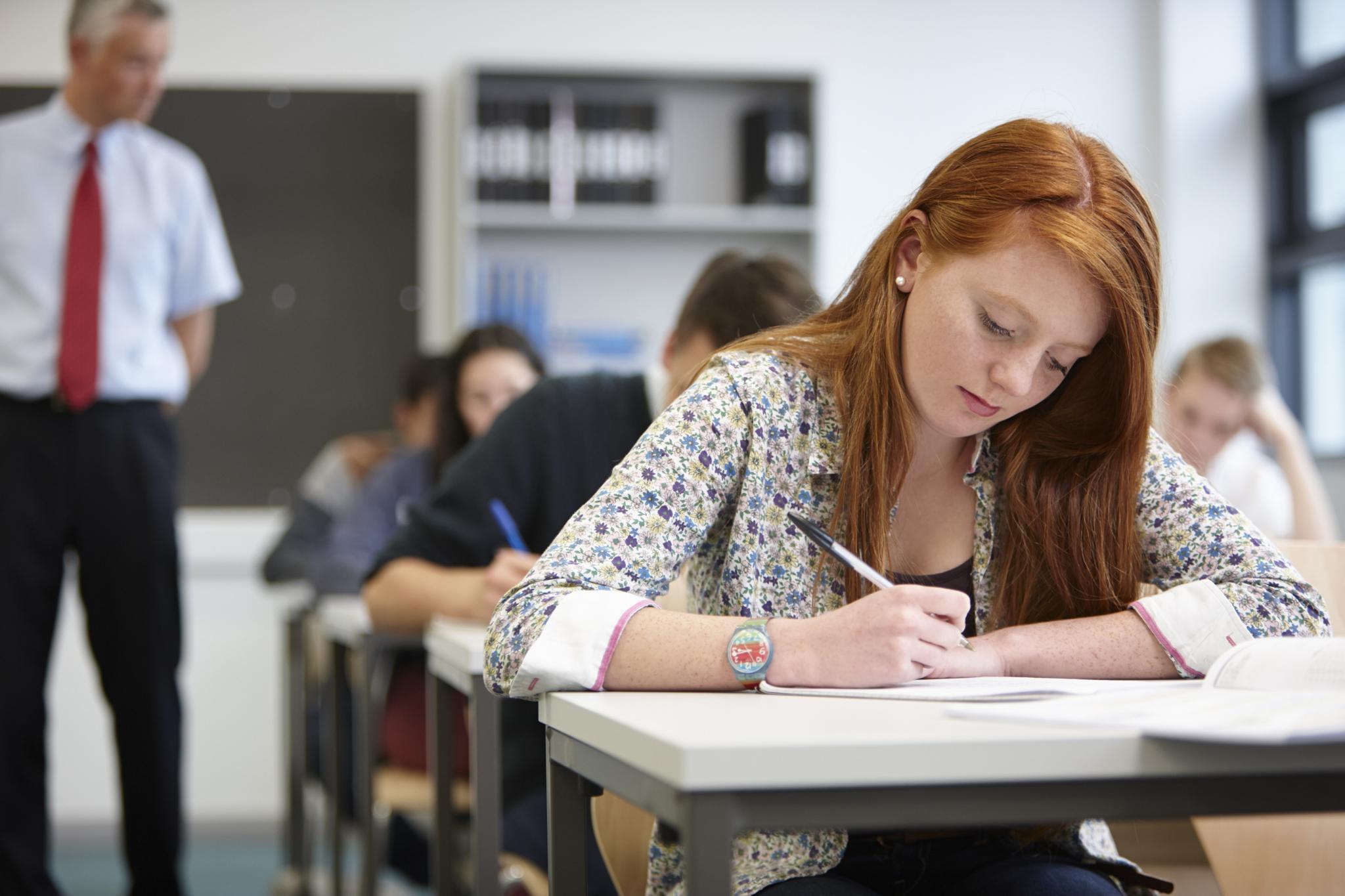 Teacher watching over teenagers in classroom - stock photo