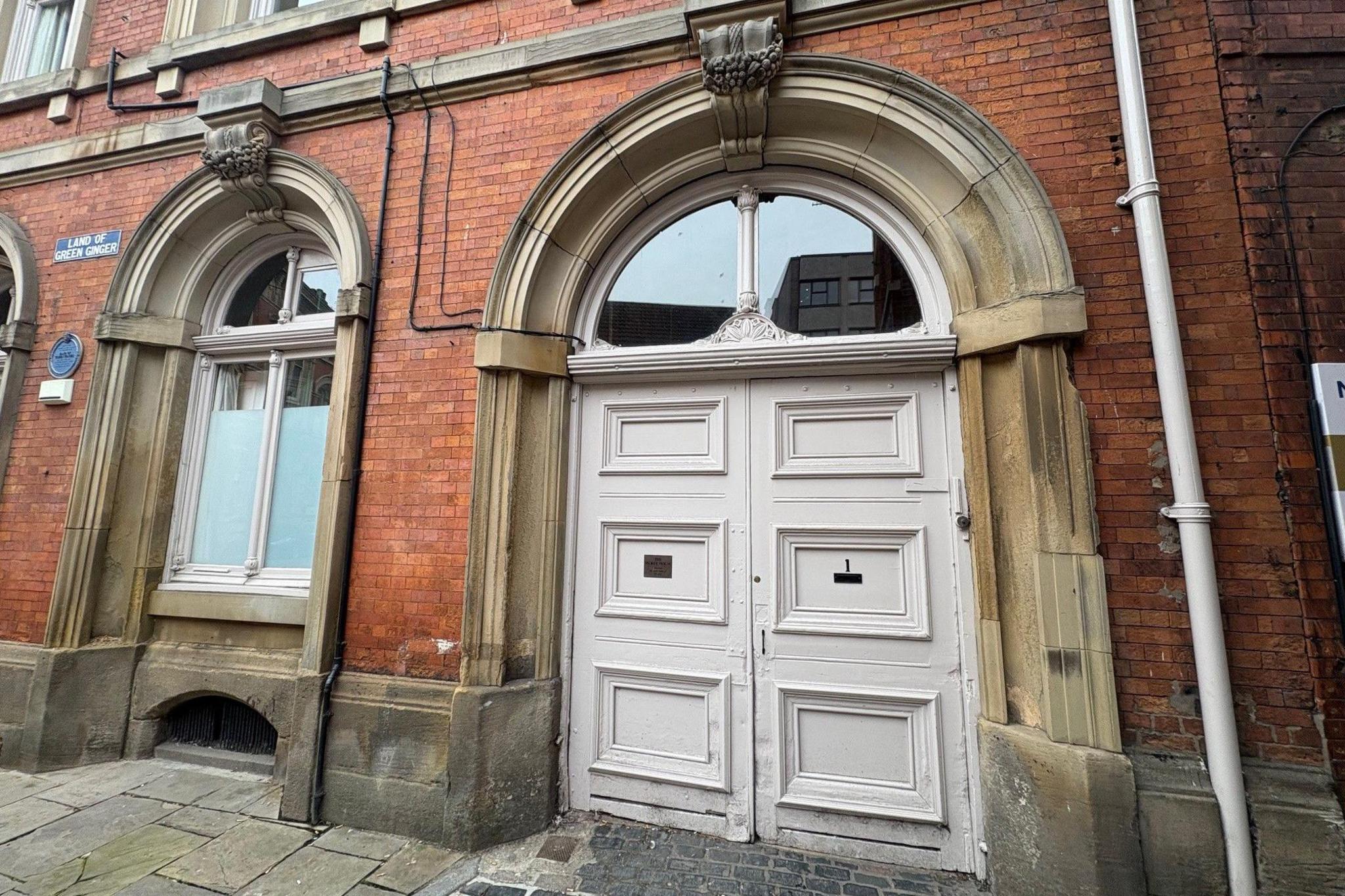Two large white double doors. One the front of one of the doors is a brass plaque stating 'The Secret House'