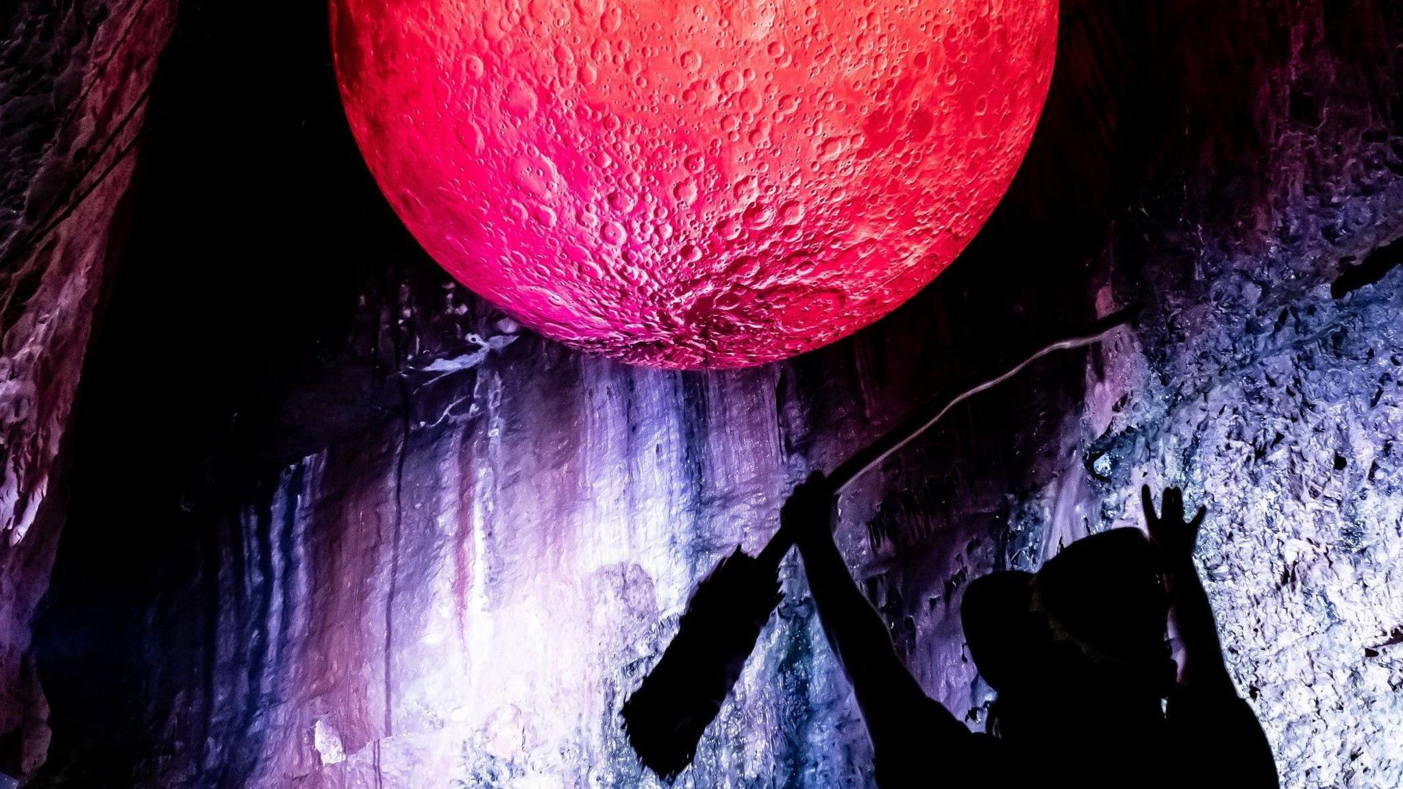 A woman dressed as a witch is silhouetted against a red "blood moon" artwork in Wookey Hole caves near Cheddar in Somerset