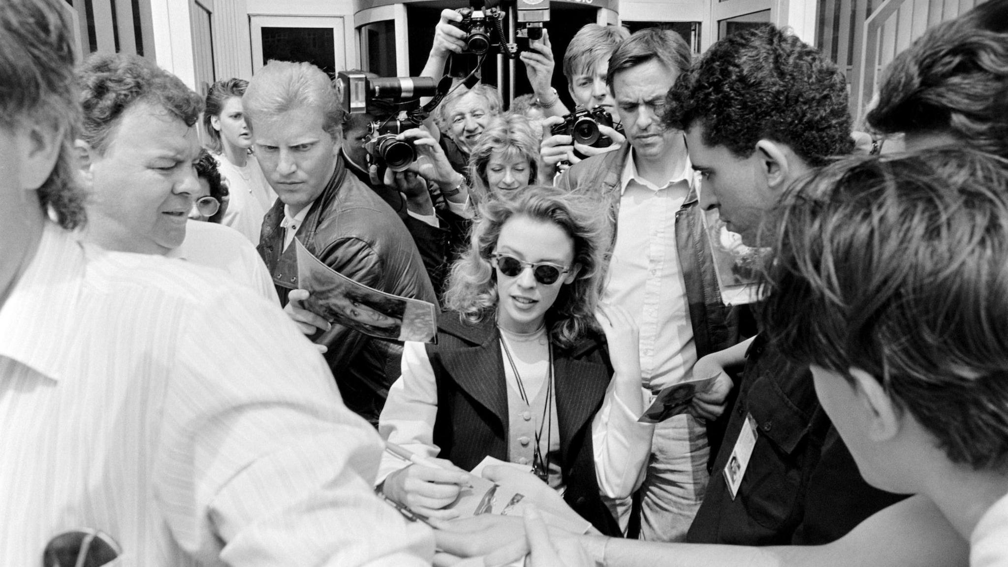 A black and white photo shows Kylie Minogue besieged by fans and the paparazzi, outside the studios of Capital Radio in London, 1989