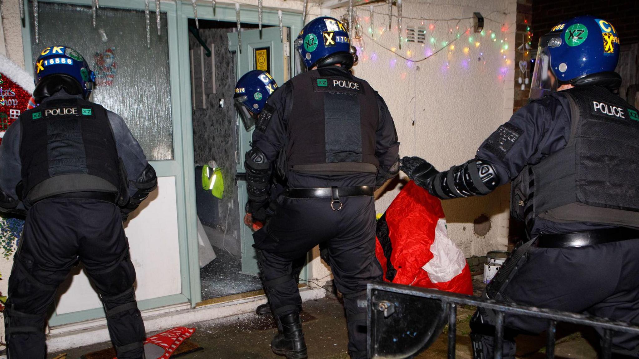 Police walk into a home where the door has been cut open, with Christmas lights seen hanging above the property and a deflated blow-up Santa seeing lying on the ground. 