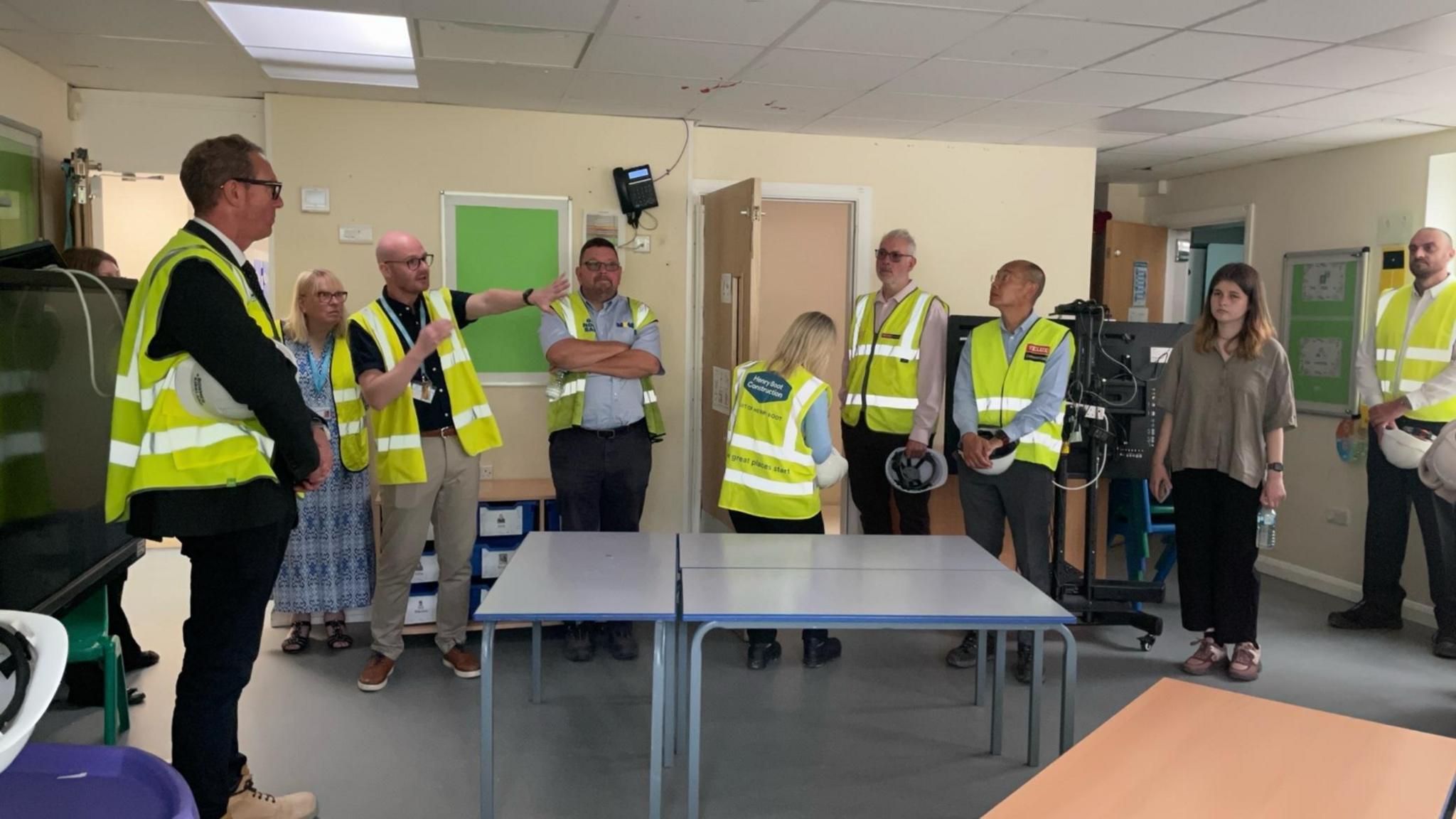 Volunteers from the contractors are stood listening to Sam MacDonald in one of the school's classrooms during a tour of its facilities.