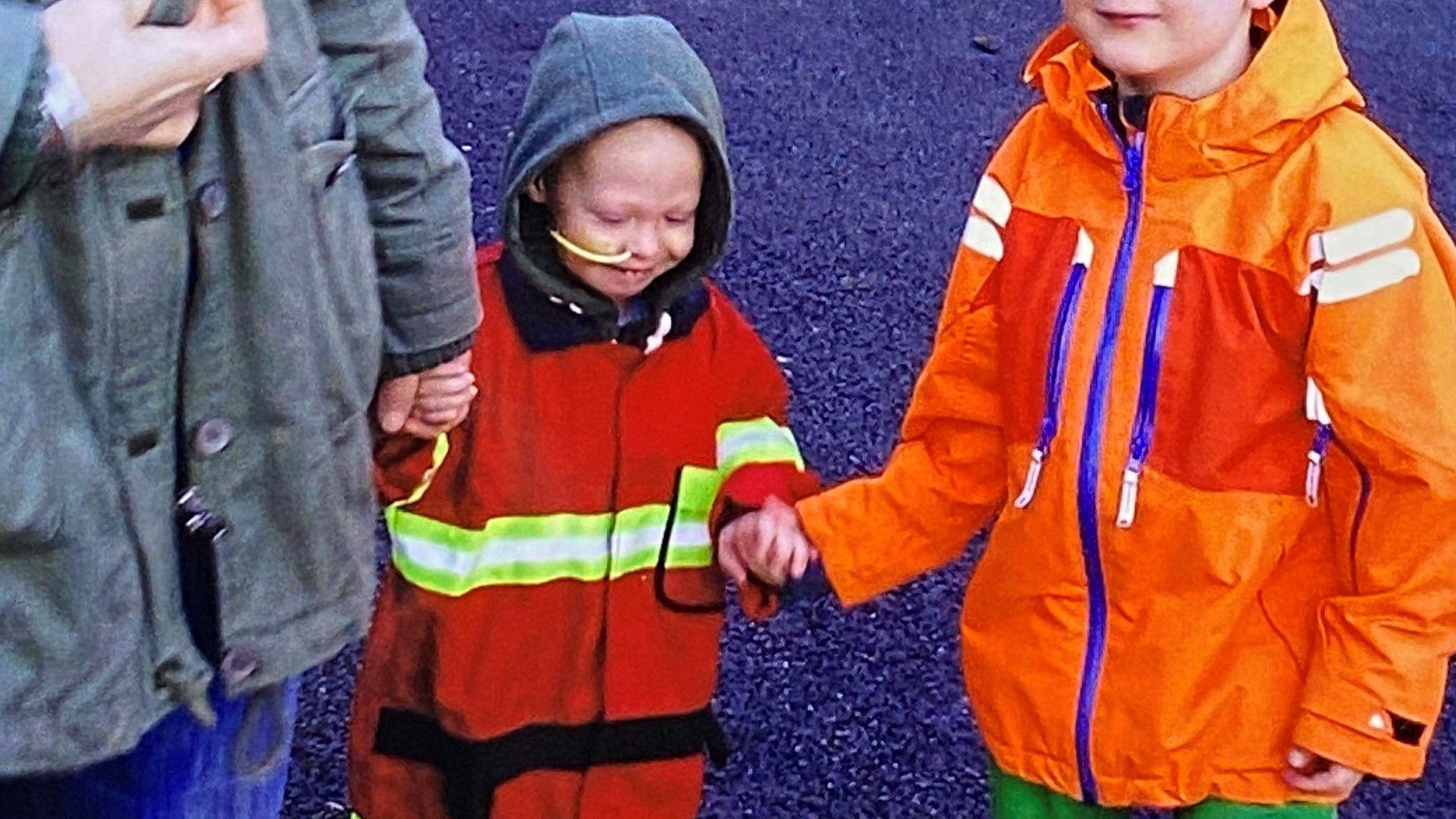 Bea and her brother when she was a toddler, being lead out of hospital by her mother and older brother wearing a feeding tube.