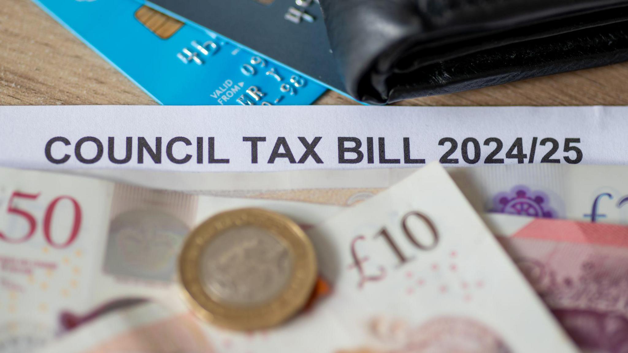 Stock image of a council tax bill, covered up with banknotes and a credit card