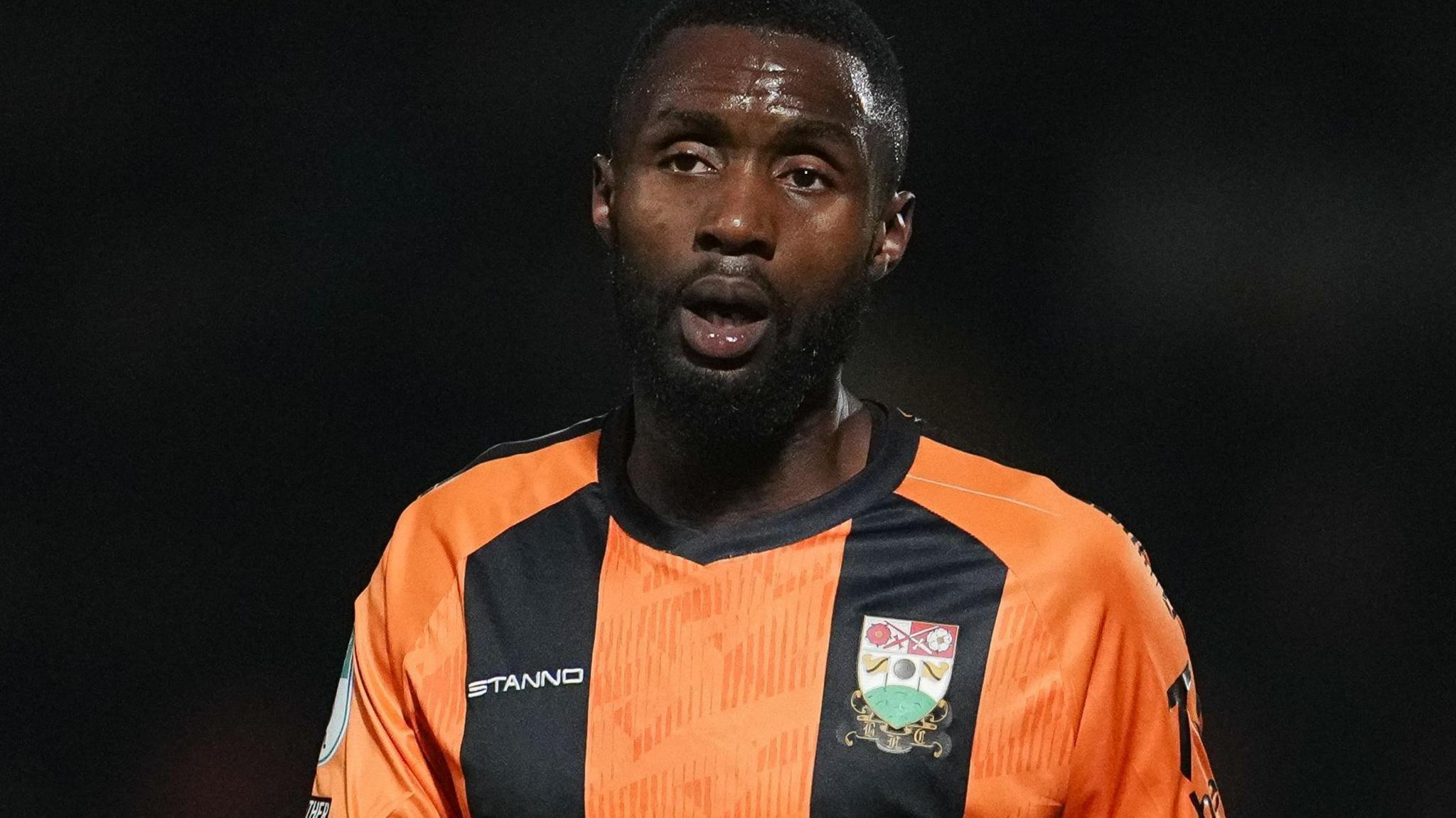 Emmanuel Osadebe wearing orange and black-striped shirt.