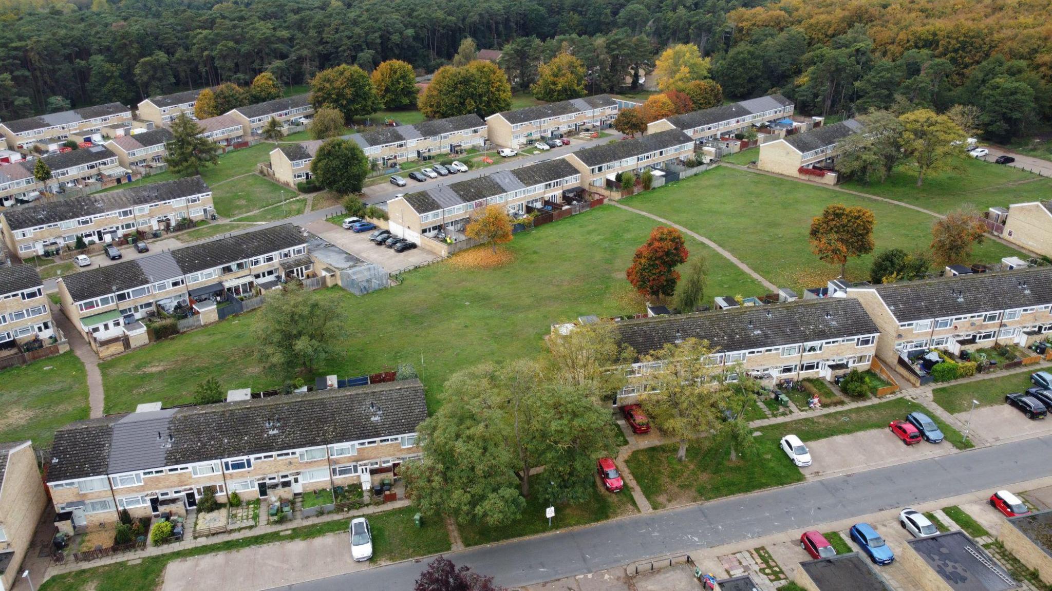 A bird's eye view of the estate, showing terraced houses, with green space and lots of trees. There are parked cars in parking bays.