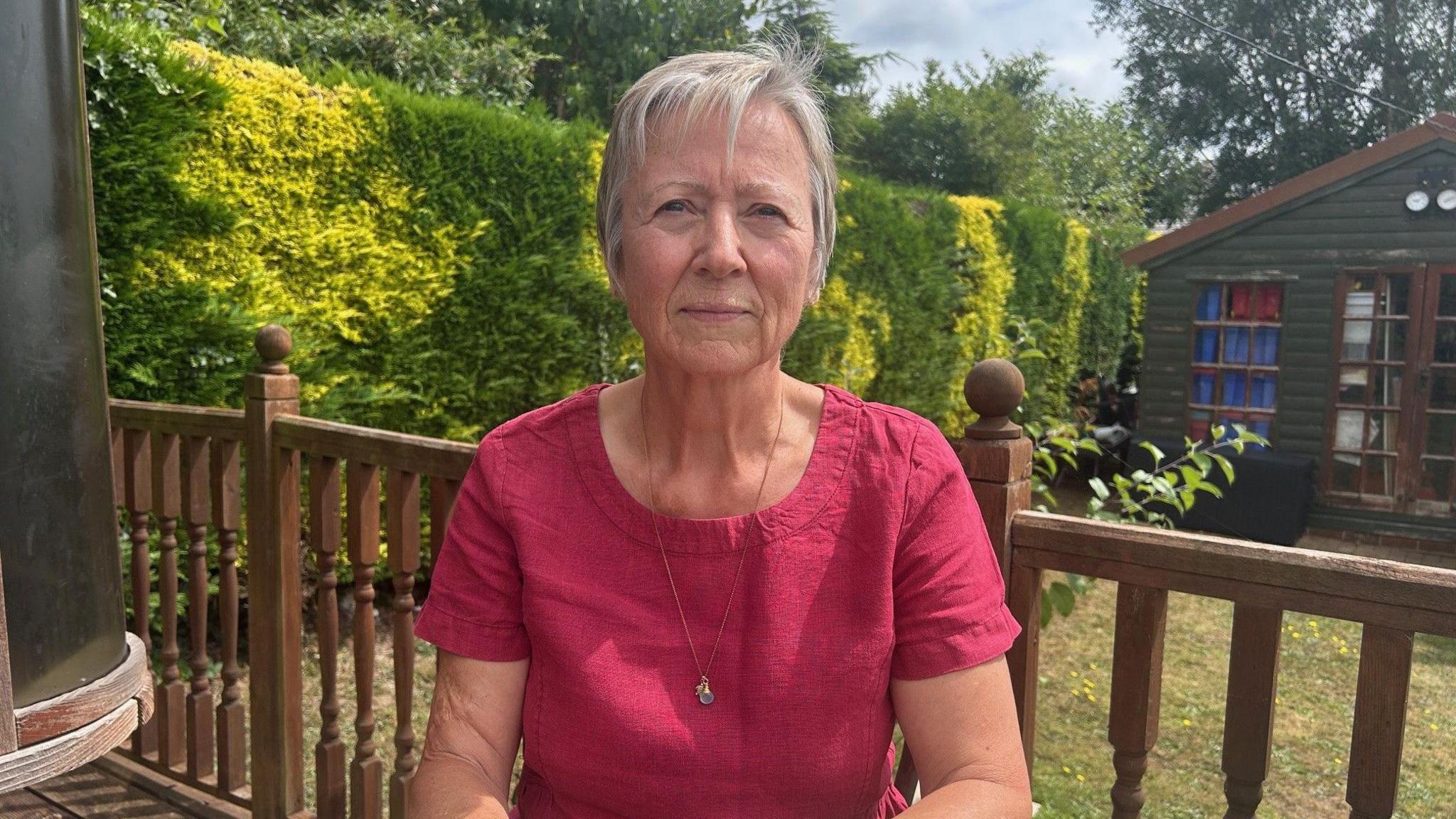 A woman in a dark pink top and grey hair sitting at a garden table