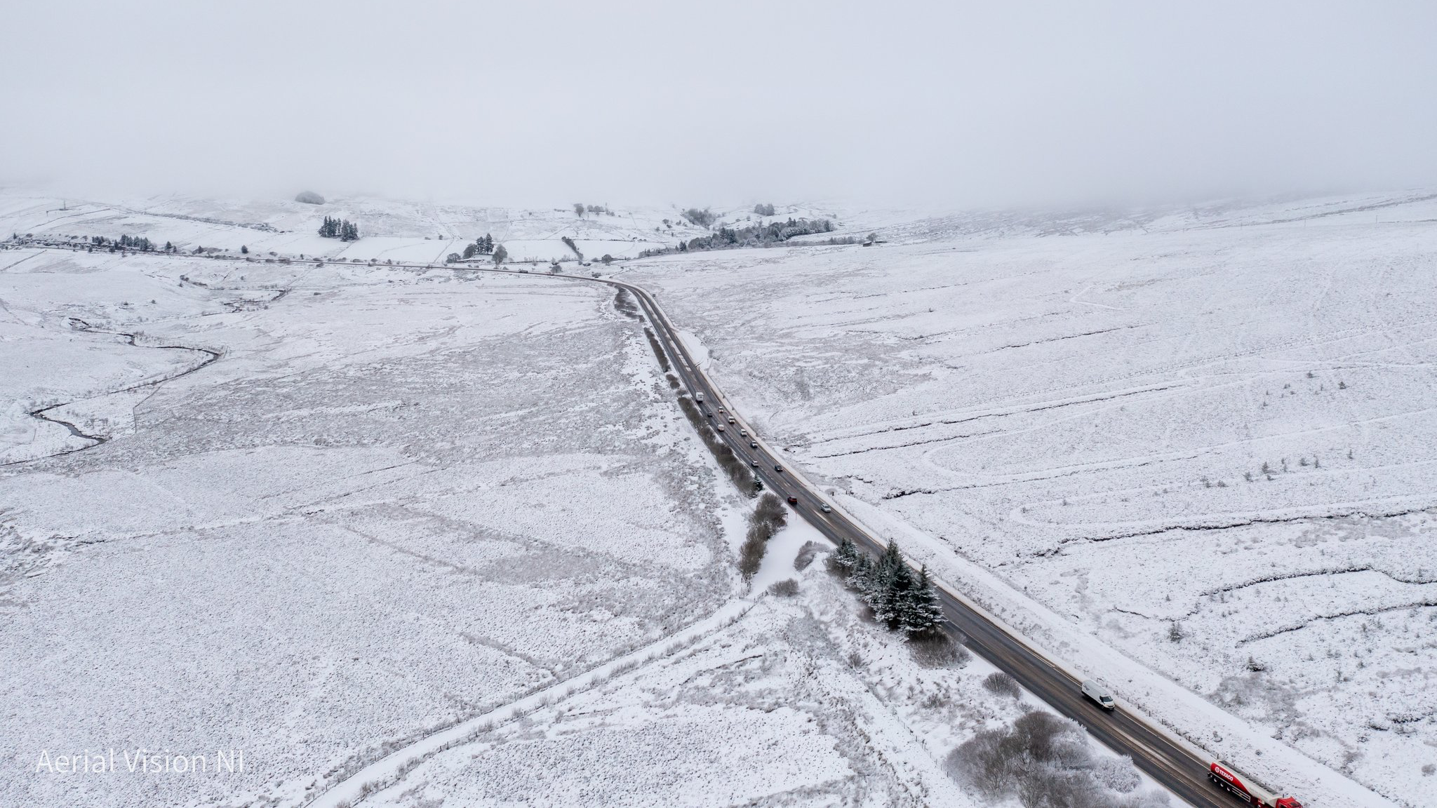 An aeriel shot of the Glenshane pass in Northern Ireland. Snow covers the surrounding fields which the road bisects. Traffic can be seen on the road