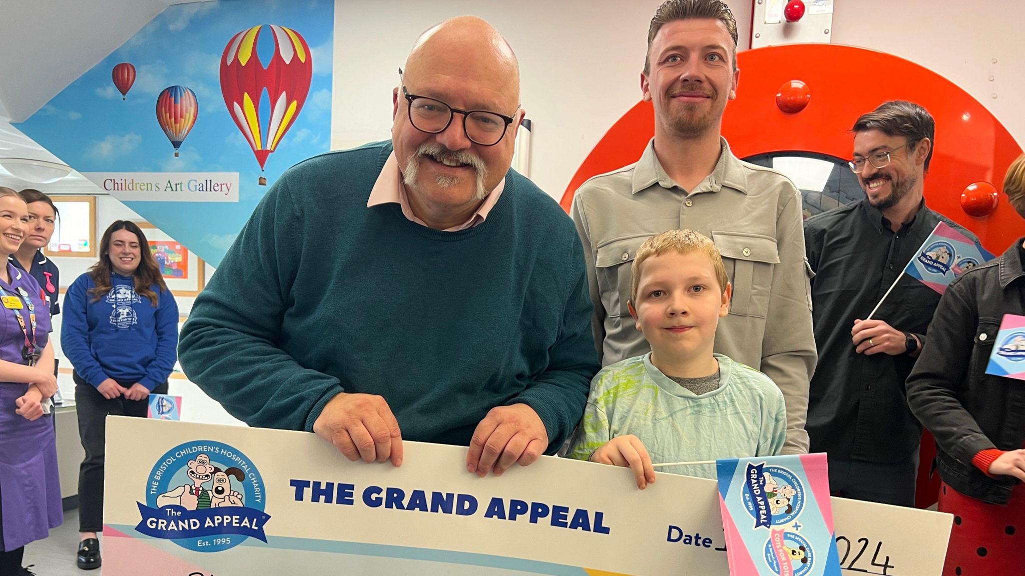 Harry Studley stands next to his father and consultant paediatric neurosurgeon Michael Carter at the Bristol Children's Hospital as he presents him with a cheque for £8,000 for the Grand Appeal.