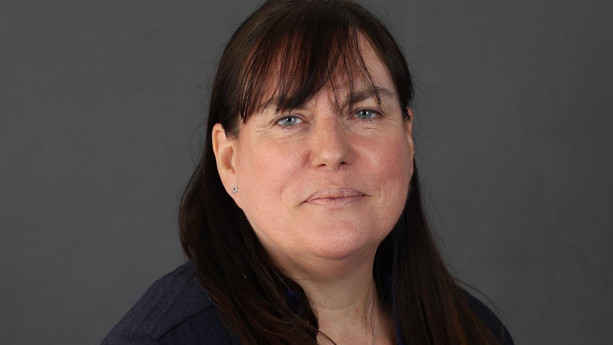 A dark-haired woman with a dark top looks towards the camera