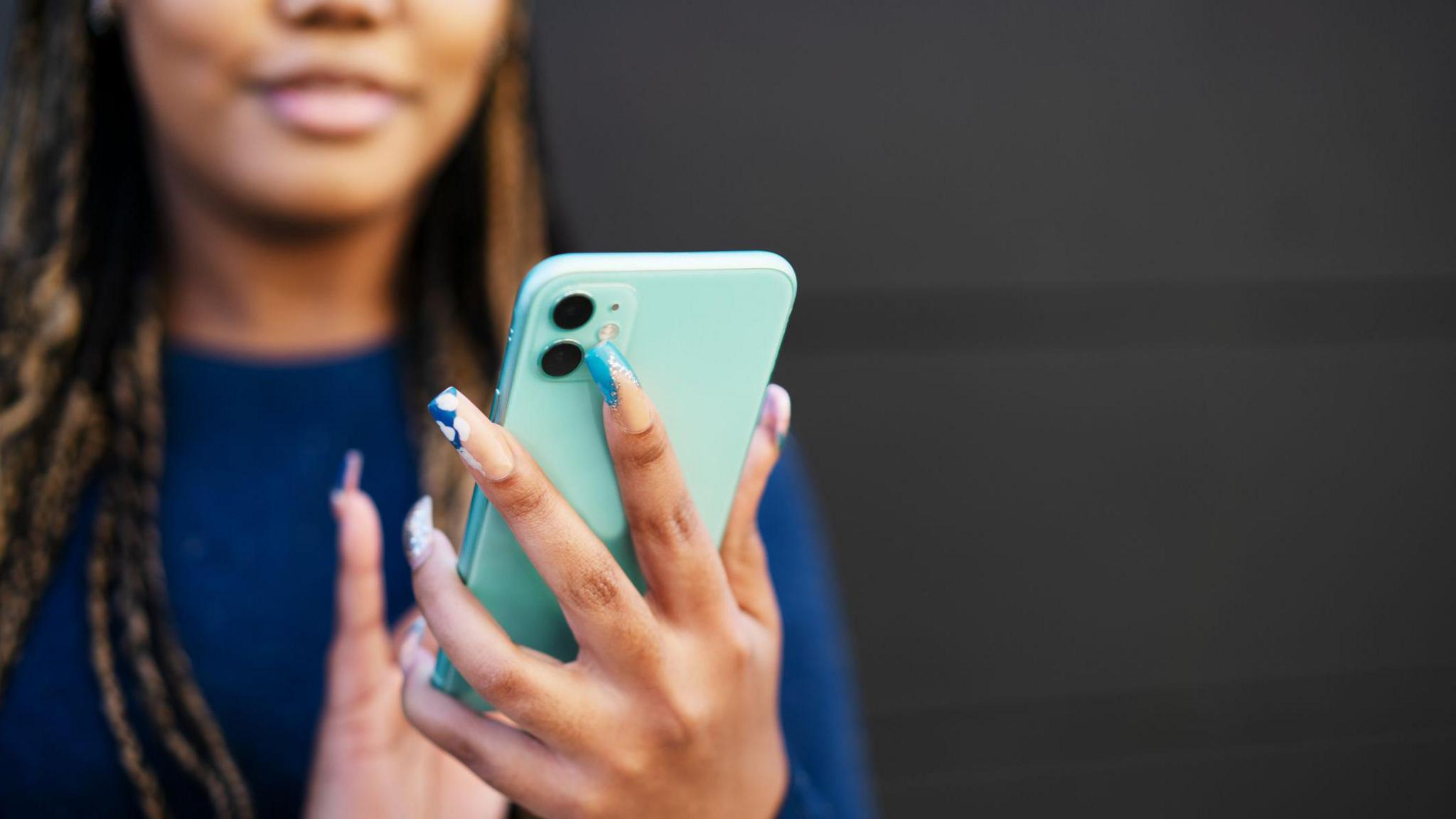 A young woman wearing a dark blue top looks at her smartphone