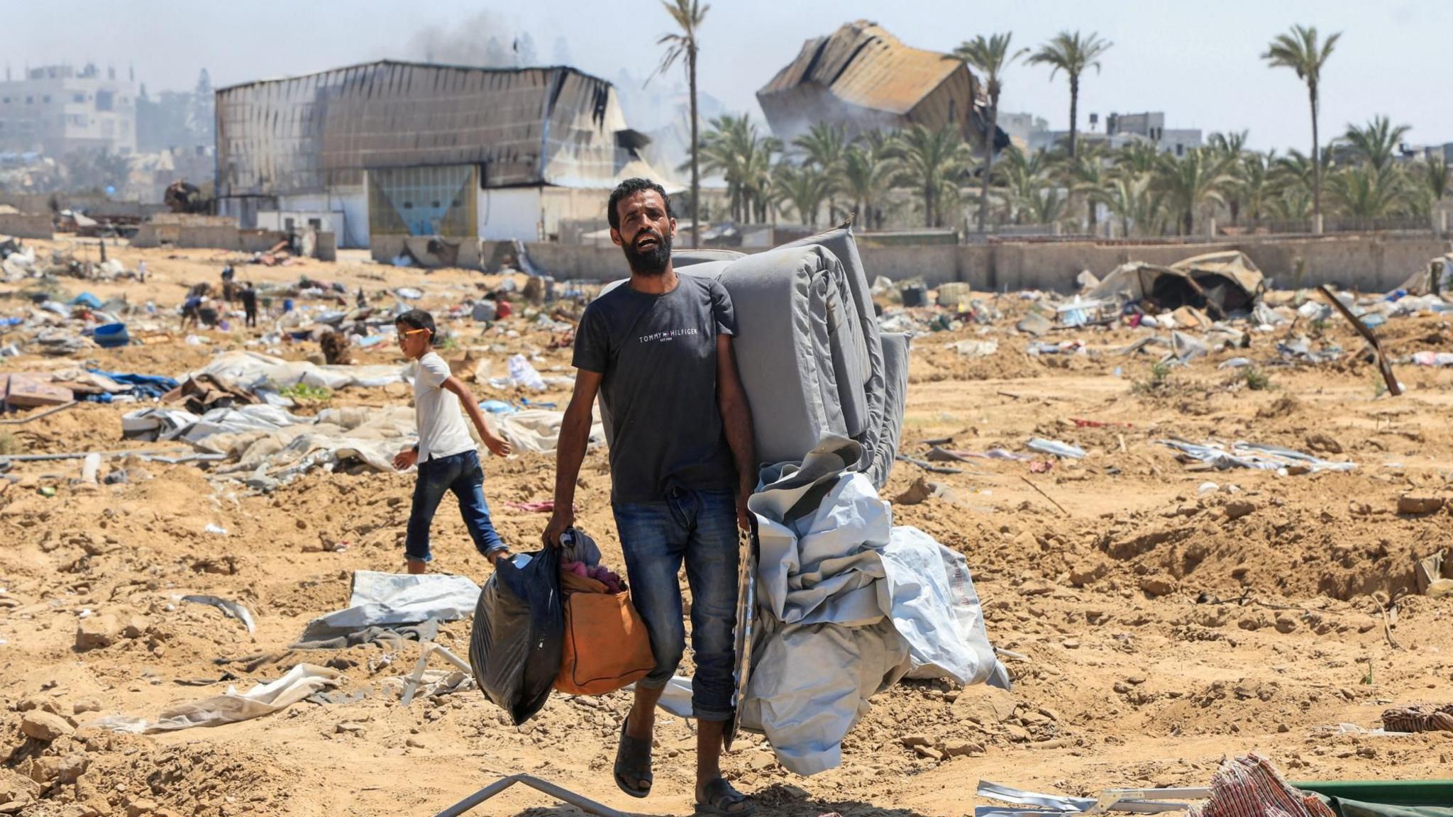 A displaced Palestinian man carries his possessions following an Israeli military ground operation in Deir al-Balah, central Gaza (22 July 2025)