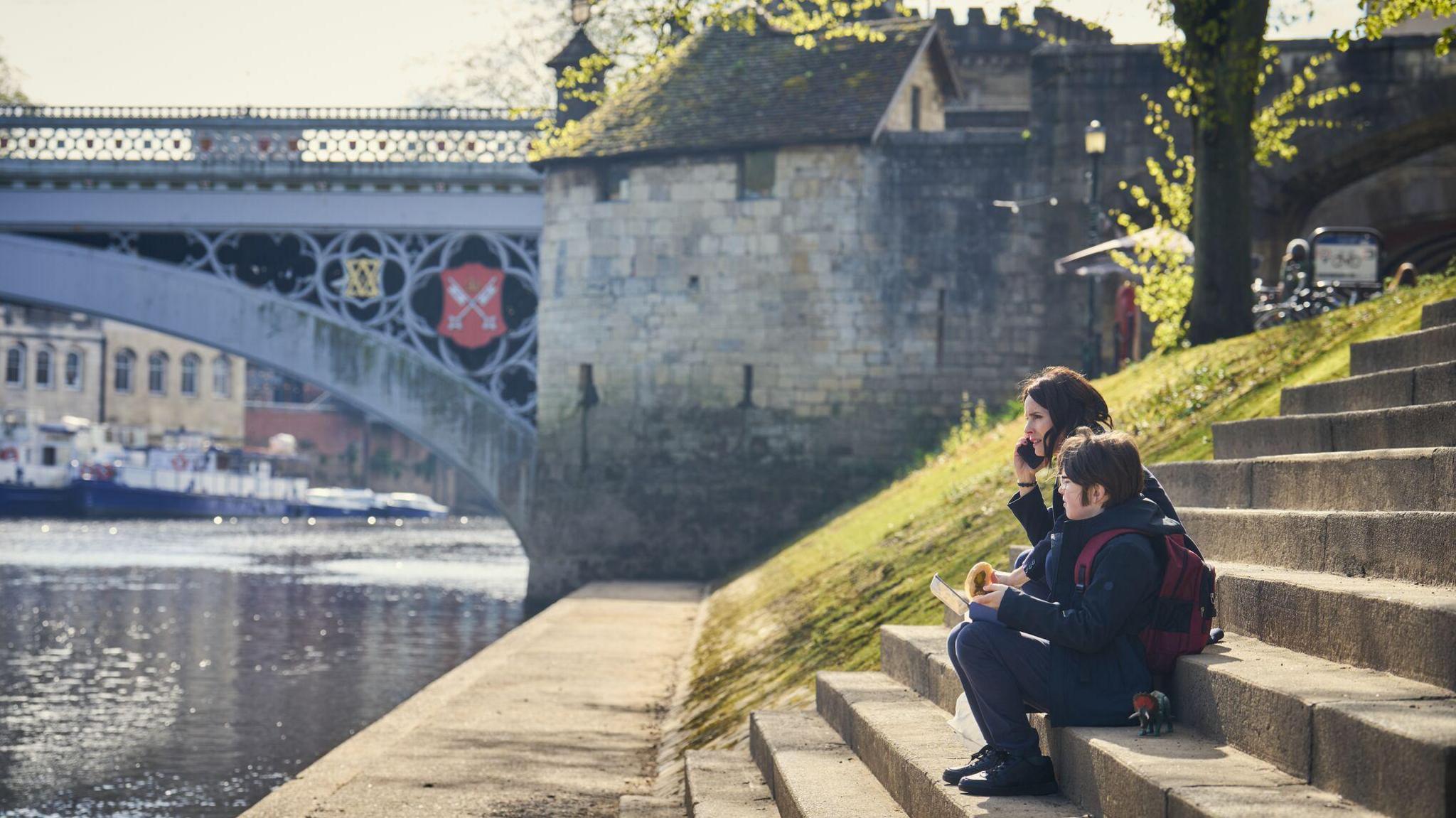 A woman and a boy sit on steps on the bank of the River Ouse in York.