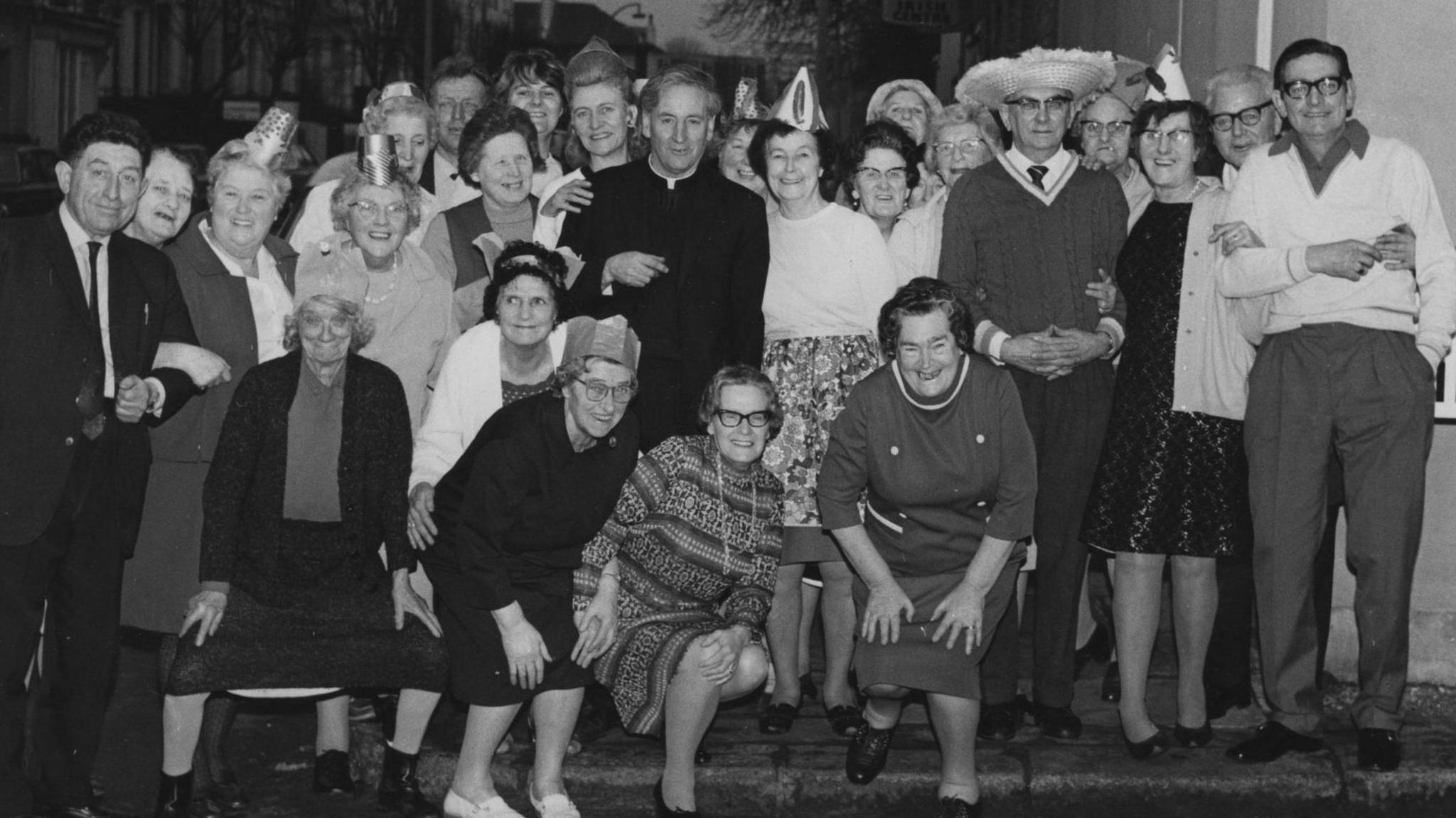 Black and white photo shows 30 people smiling at camera. Most are dressed smartly