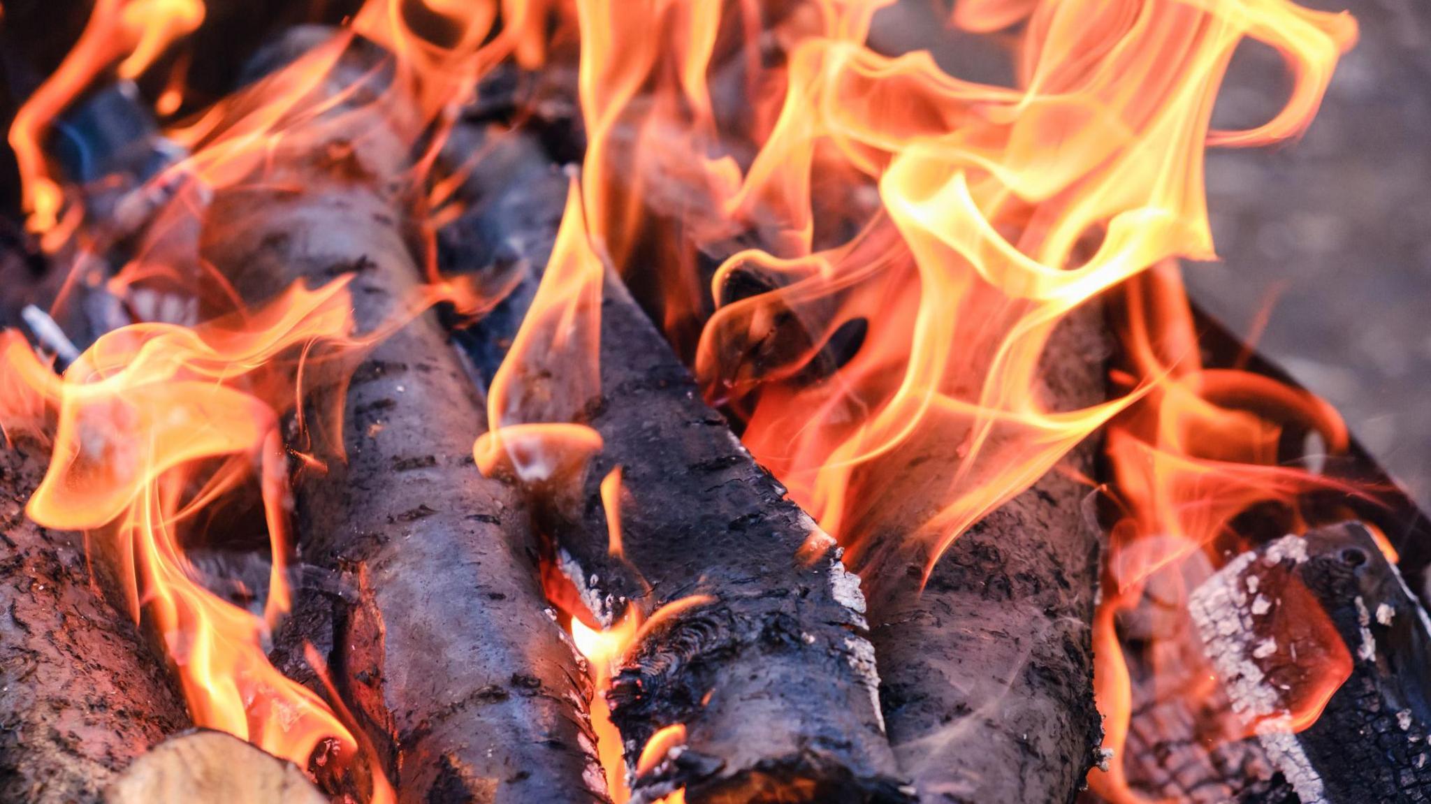 A close up picture of a camp fire or barbecue with logs burning and bright orange flames dancing around them 