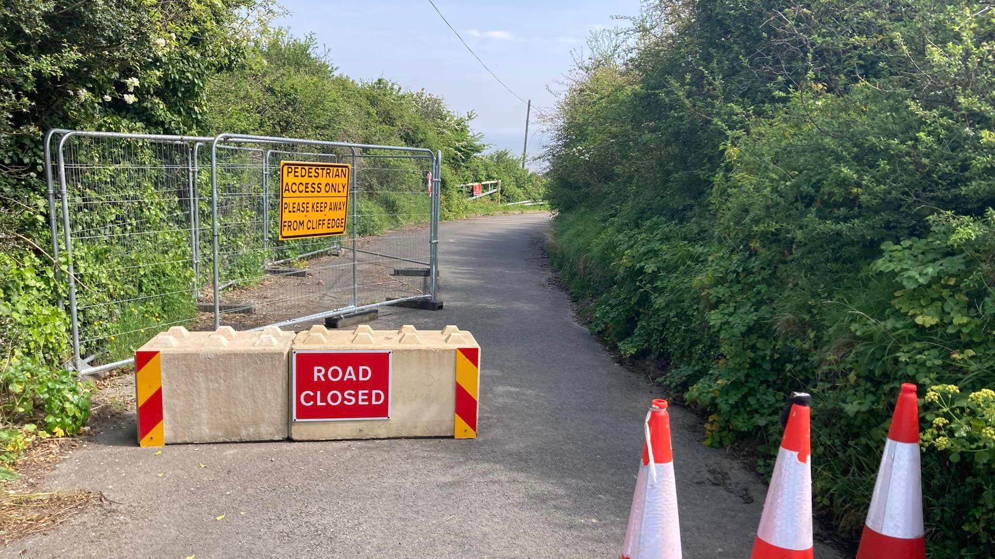 Road closed sign on narrow cliff road with cones and barriers saying "Pedestrian Access"