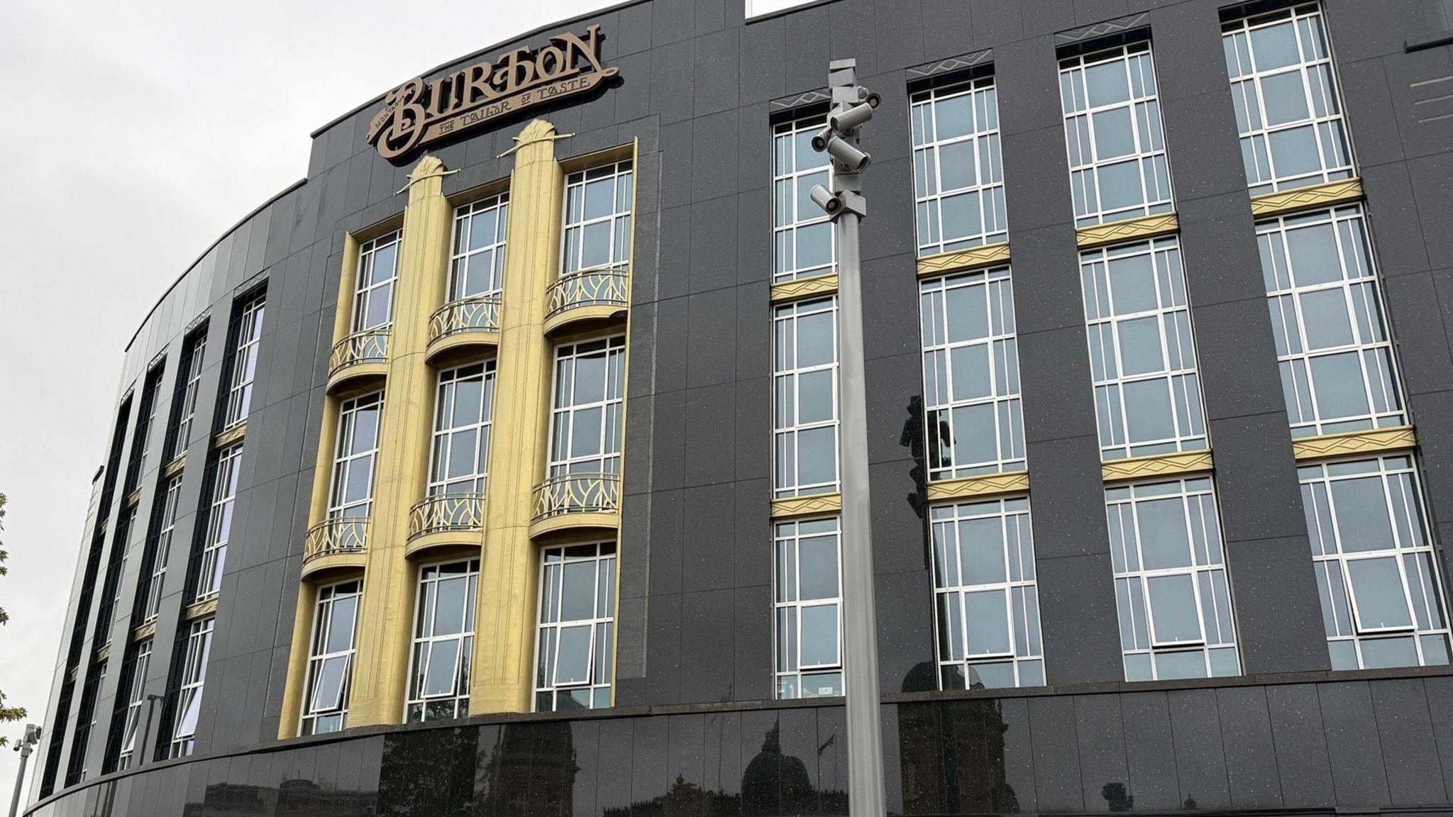 A large corner building restored to its original 1930s look. Black granite cladding cover the building which has a number of long windows. The centre of the building is painted gold.