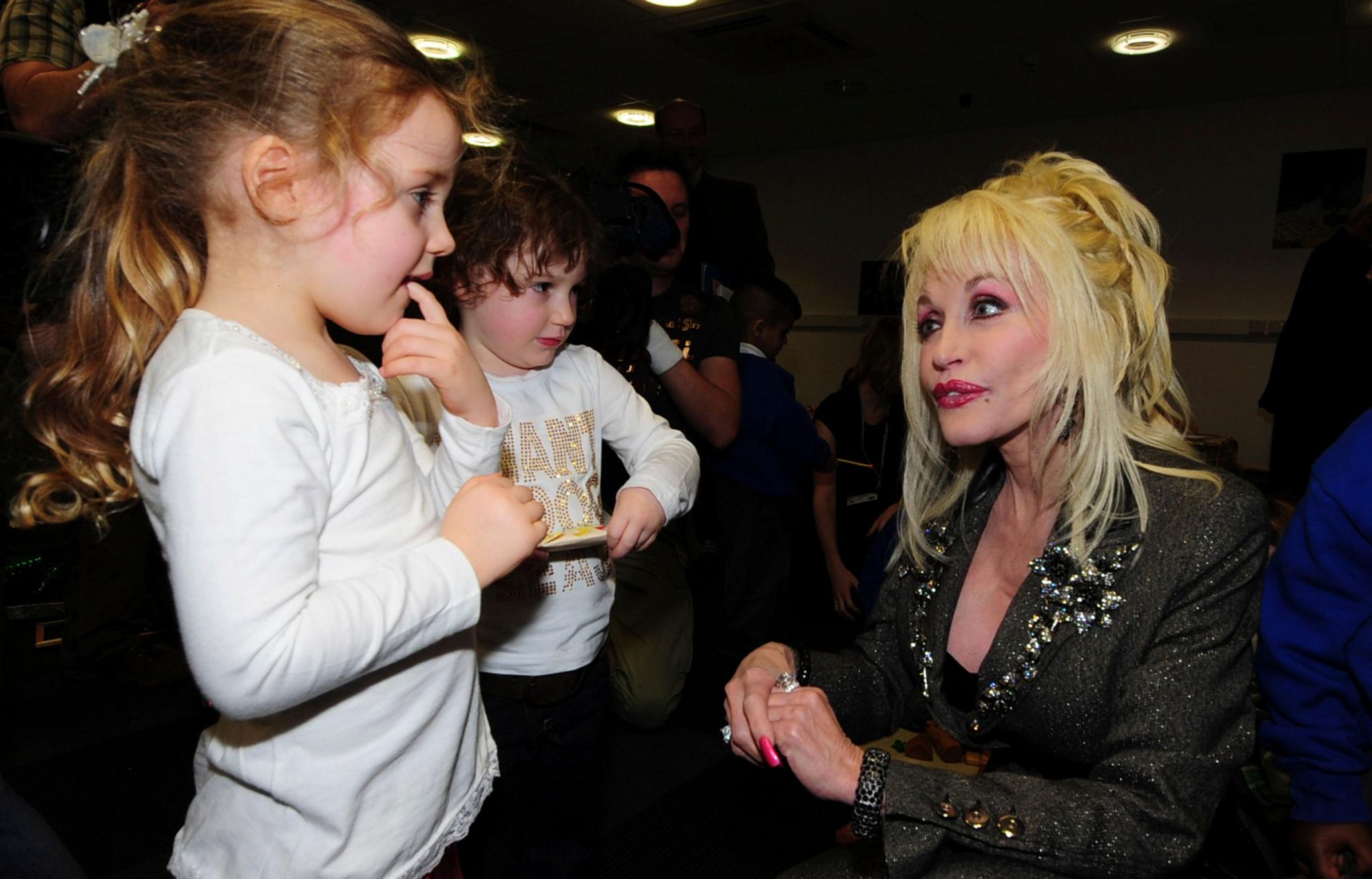 Parton kneels as she speaks to two young children at the launch of her Imagination Library book project in 2007