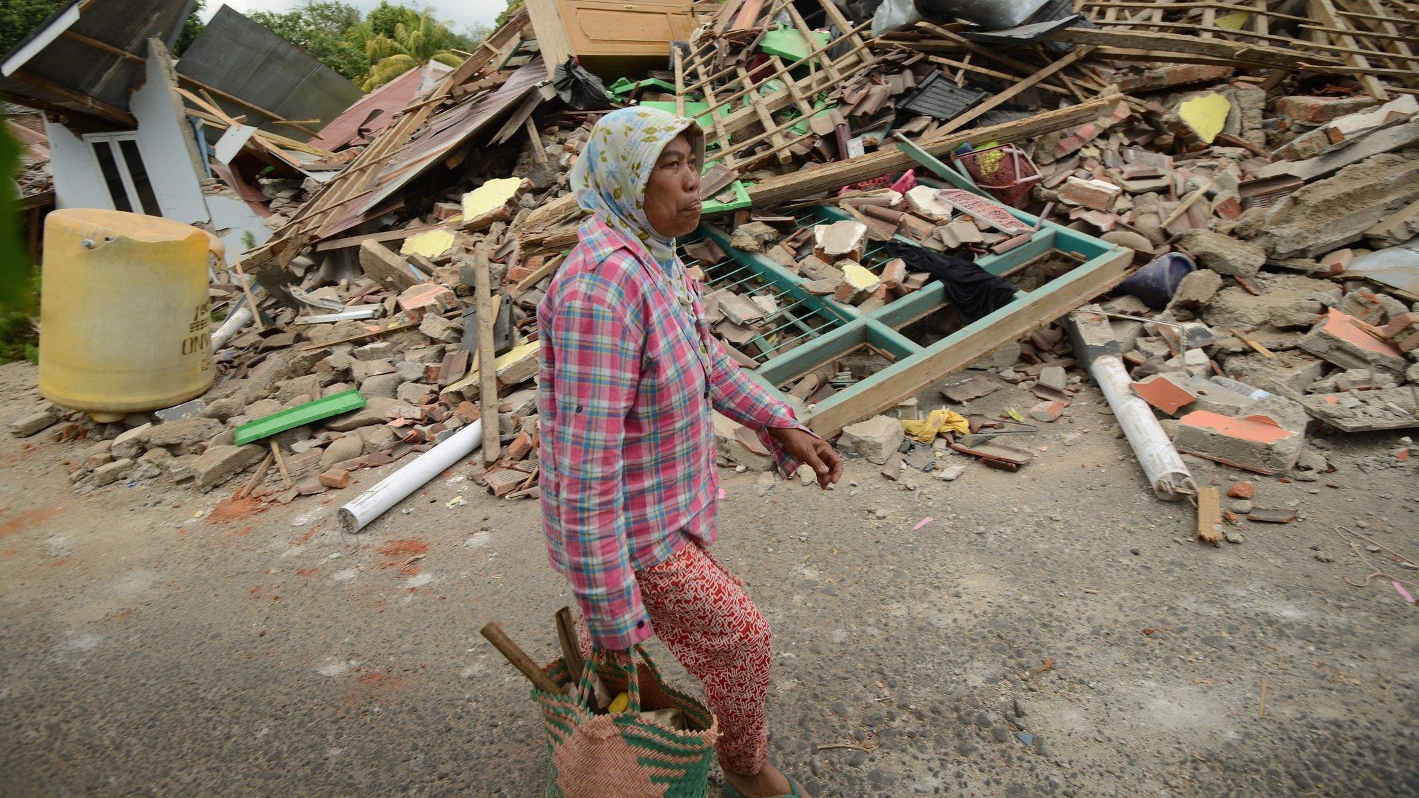 A woman walks past collapsed houses in Kayangan in northern Lombok island on August 9, 2018,